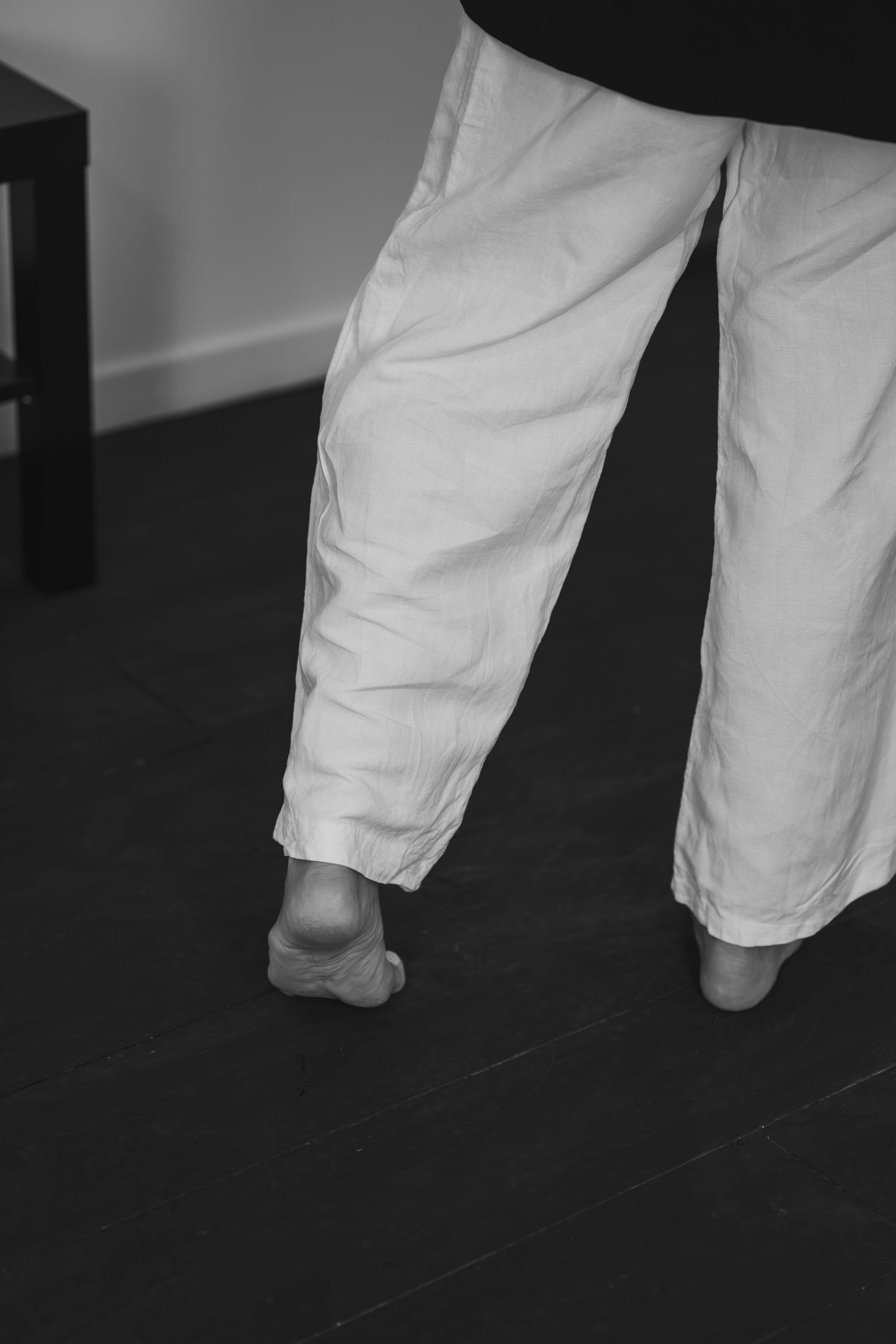 Black and white close-up photo of bare feet on a dark floor, showing a minimalist composition.