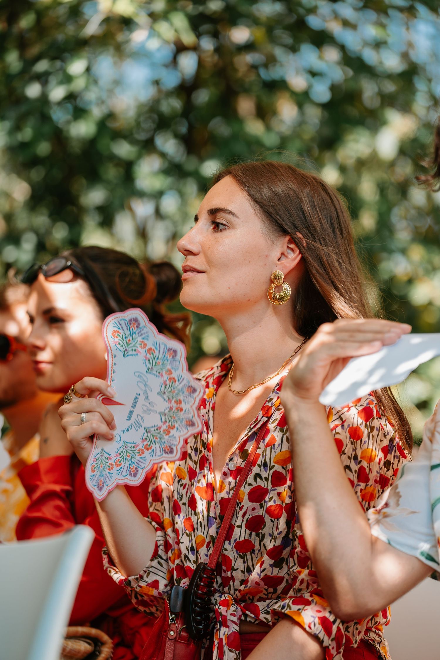 Wedding guest in a red floral dress holds up a decorative handkerchief during an outdoor celebration.