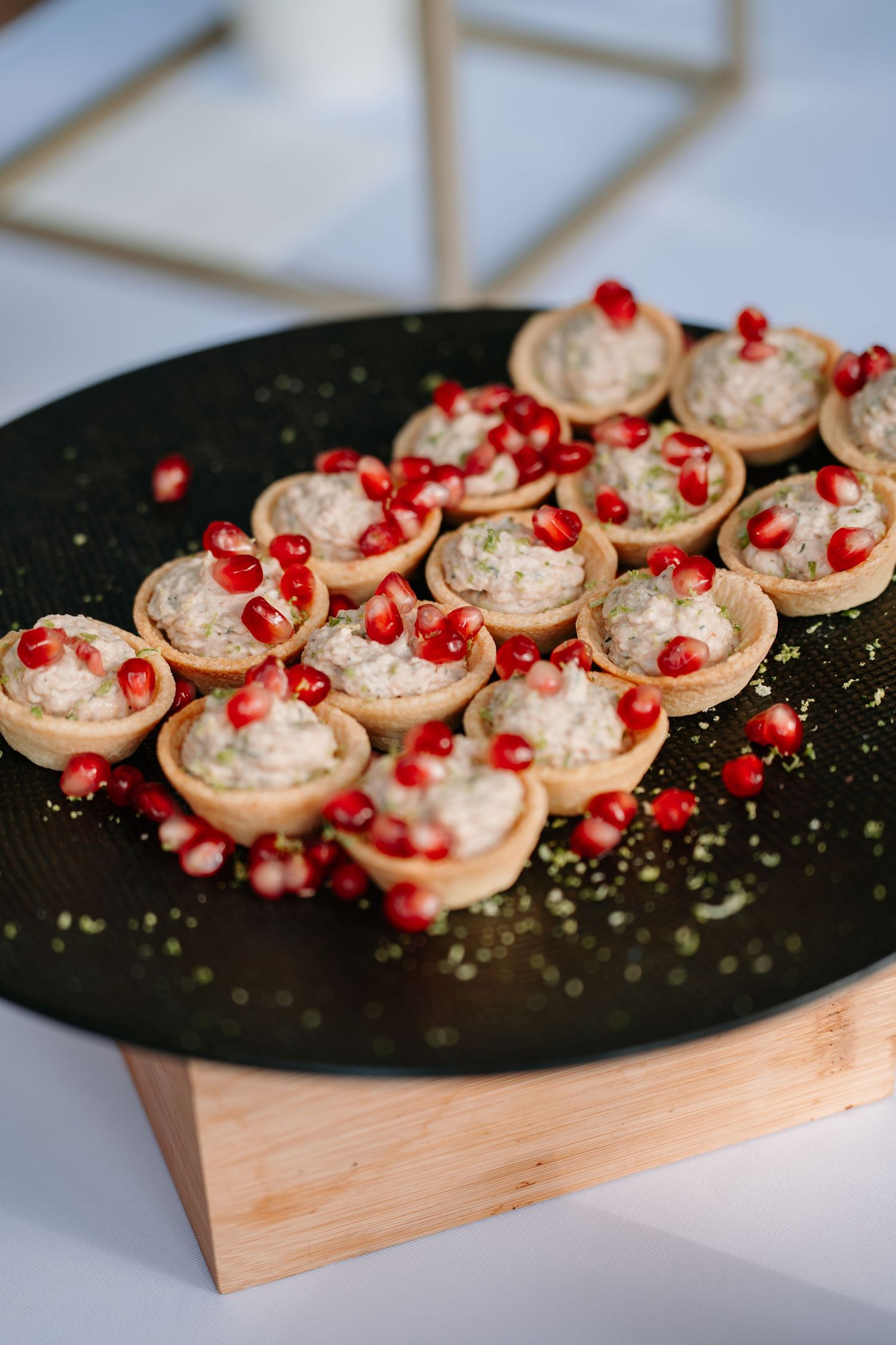Mini tart shells filled with creamy mousse and topped with fresh pomegranate seeds served on a black platter.