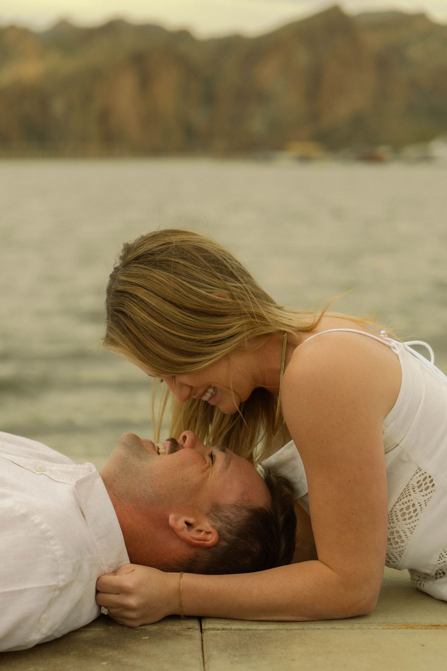 An intimate moment between a couple in white attire on a wooden dock overlooking a mountain lake.
