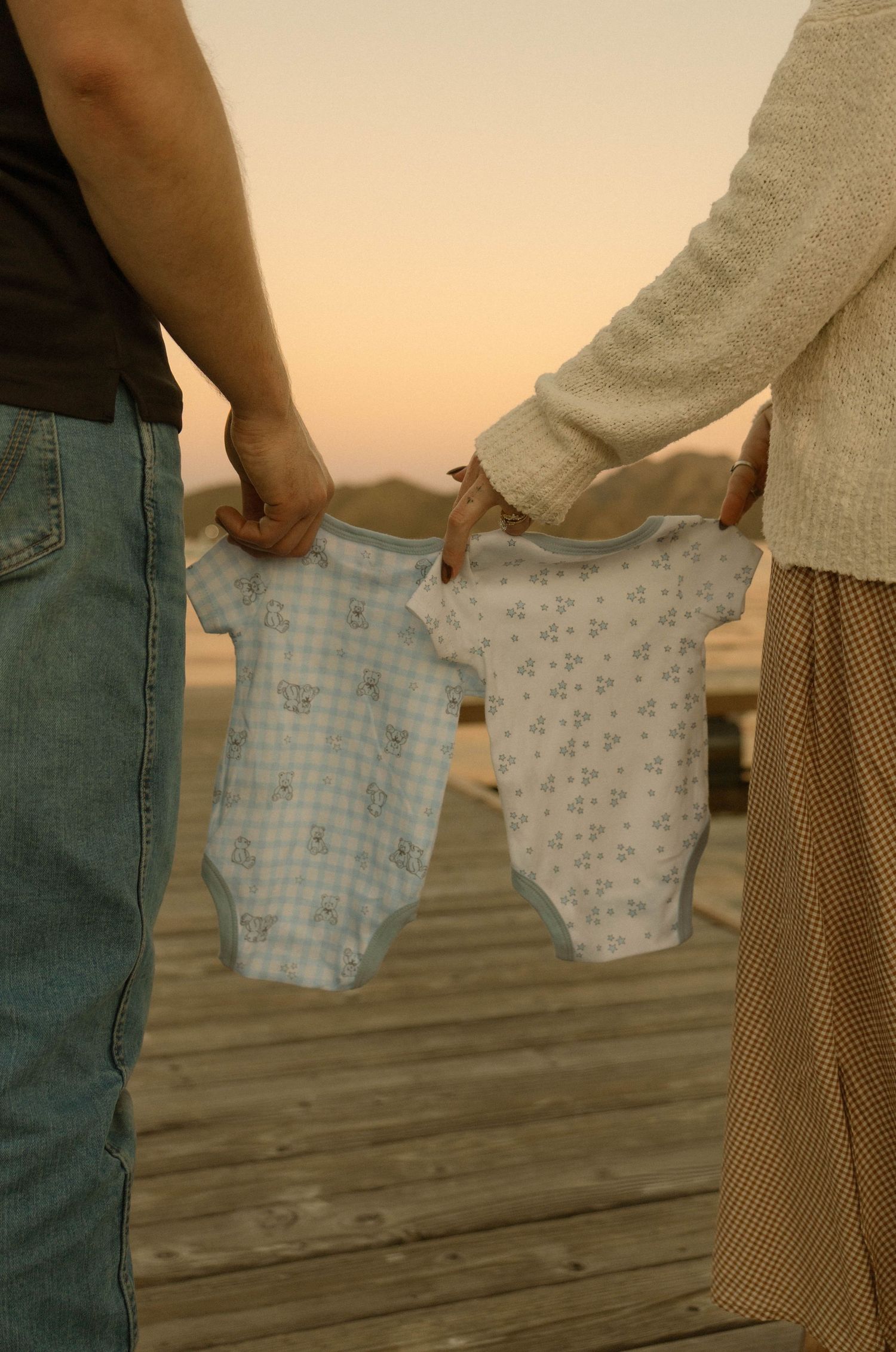 Baby clothes hanging on a clothesline against a warm sunset background.