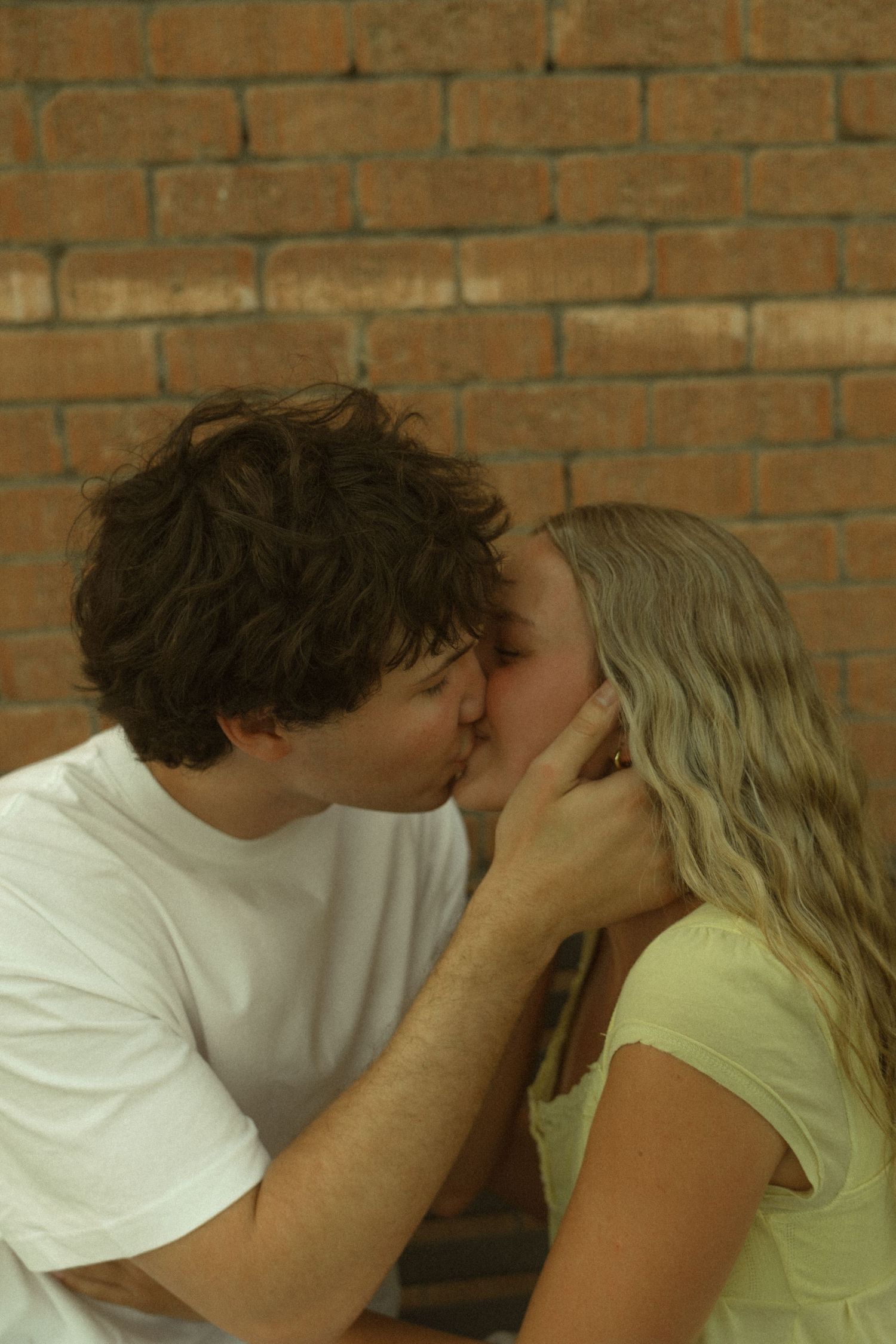 Romantic young couple sharing a kiss against a rustic brick wall background.