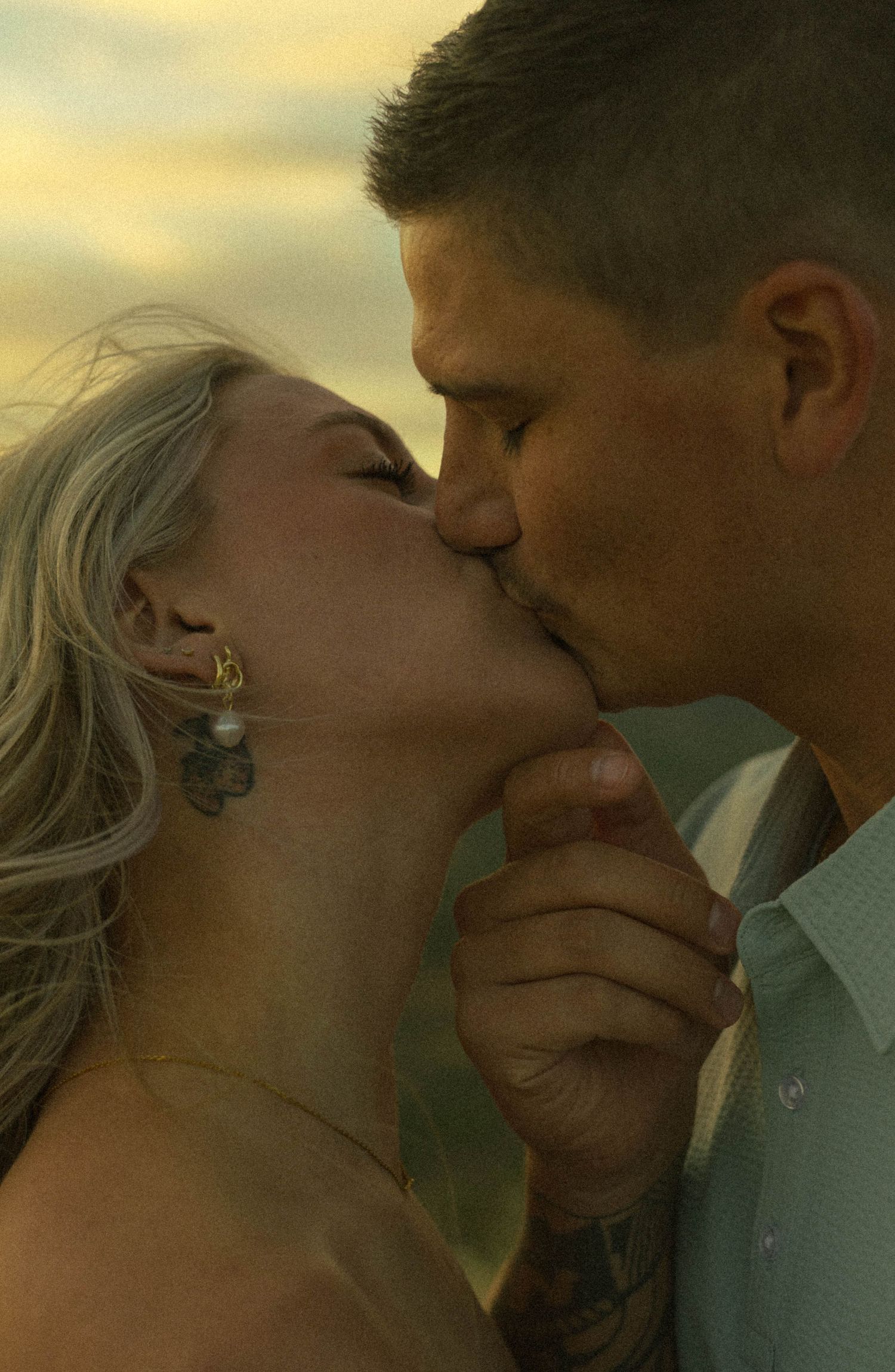 Couple sharing a passionate kiss outdoors during a beautiful golden hour sunset photo shoot.