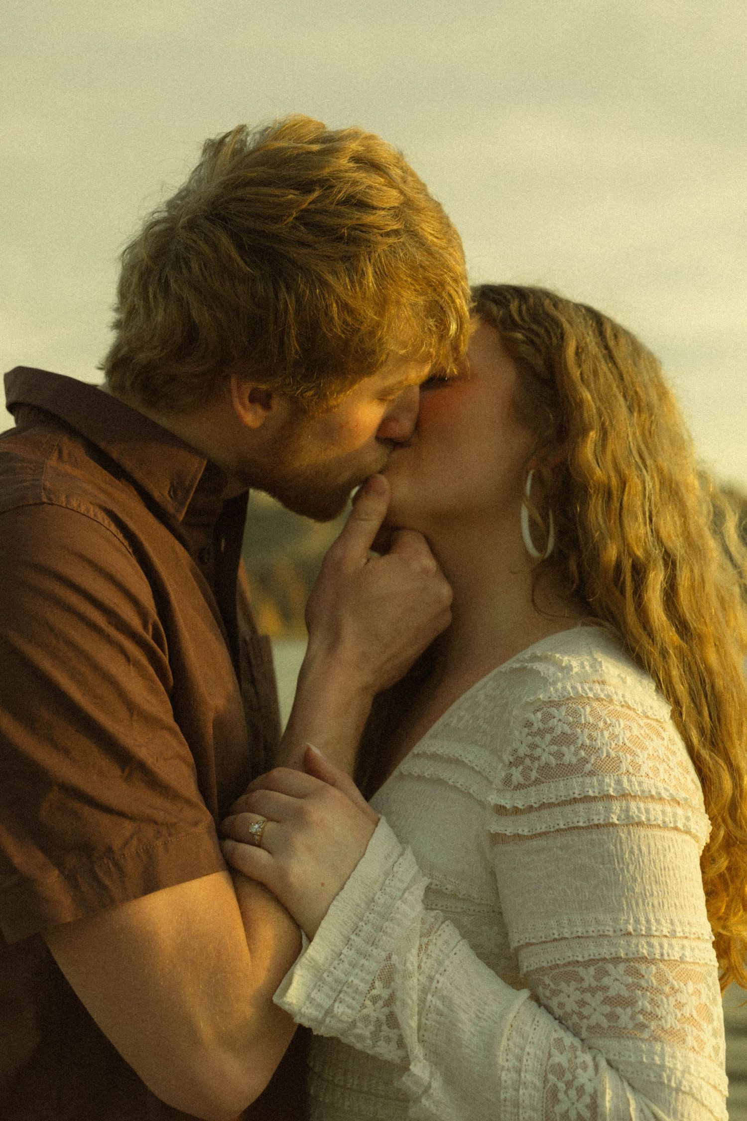 A romantic couple in warm lighting share an intimate kiss while wearing brown and white clothing.