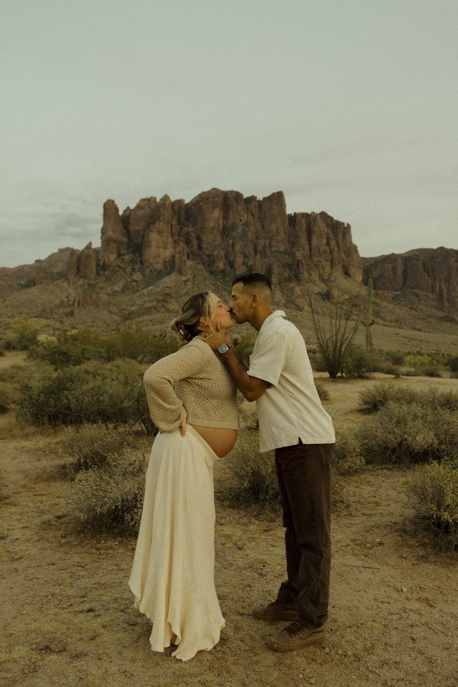 Couple sharing a kiss in the desert with rugged red rock formations in the background during an outdoor engagement session.