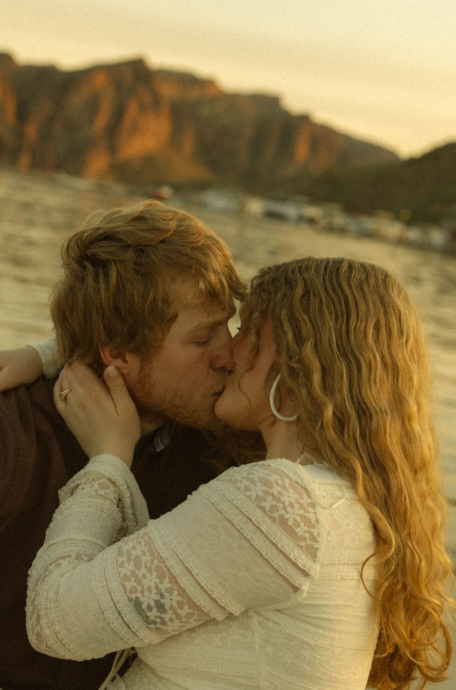 Romantic couple kissing at sunset with mountain landscape and water in the background.