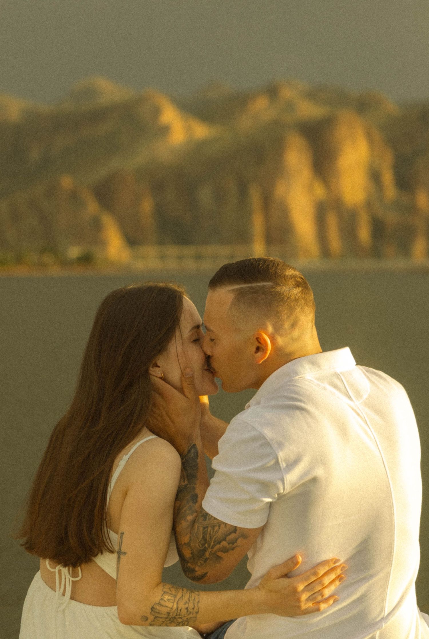 A romantic couple sharing an intimate moment at sunset with mountains and water in the background.
