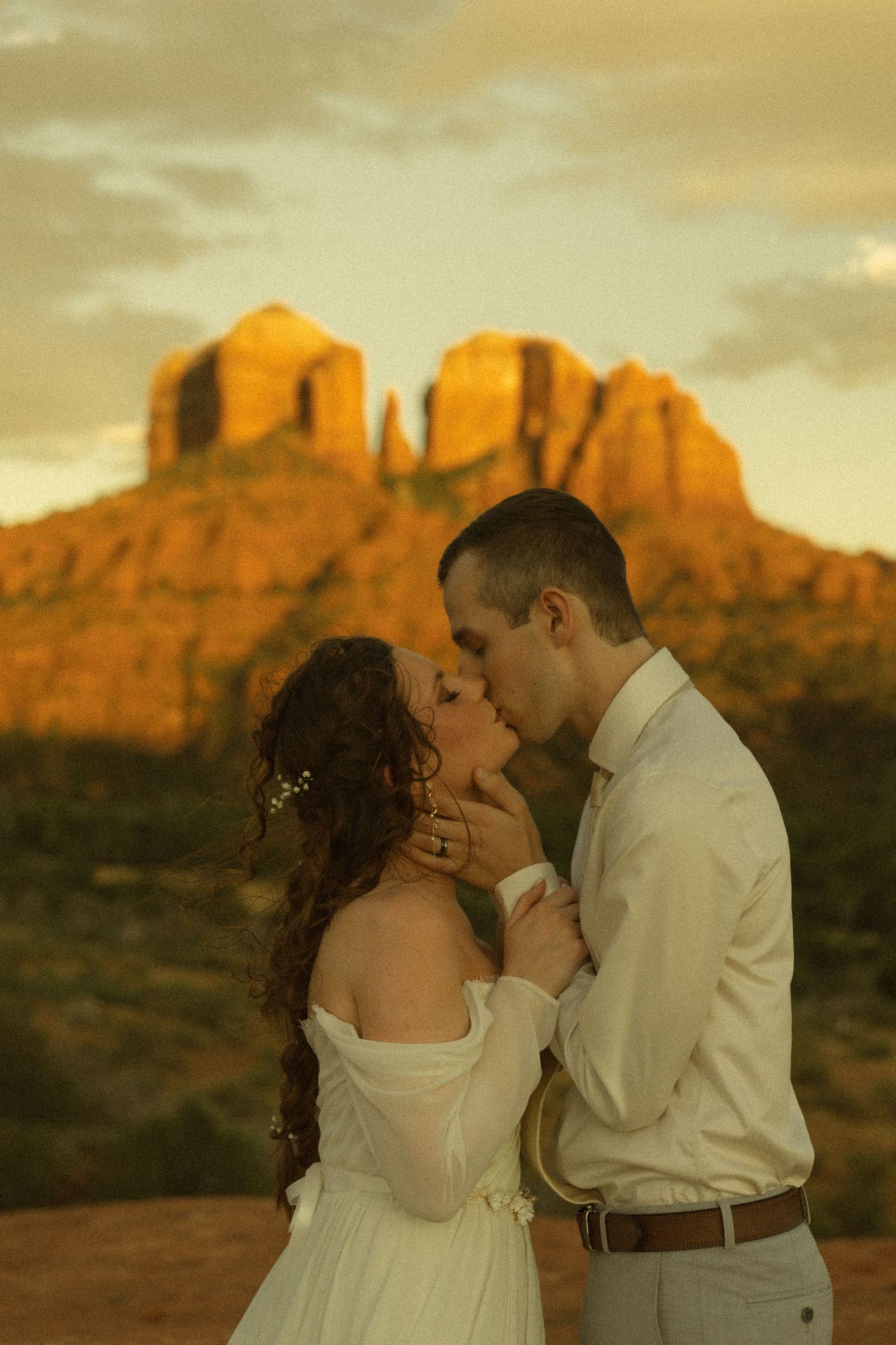 Bride and groom kissing at sunset with Cathedral Rock in Sedona, Arizona glowing golden in the background.