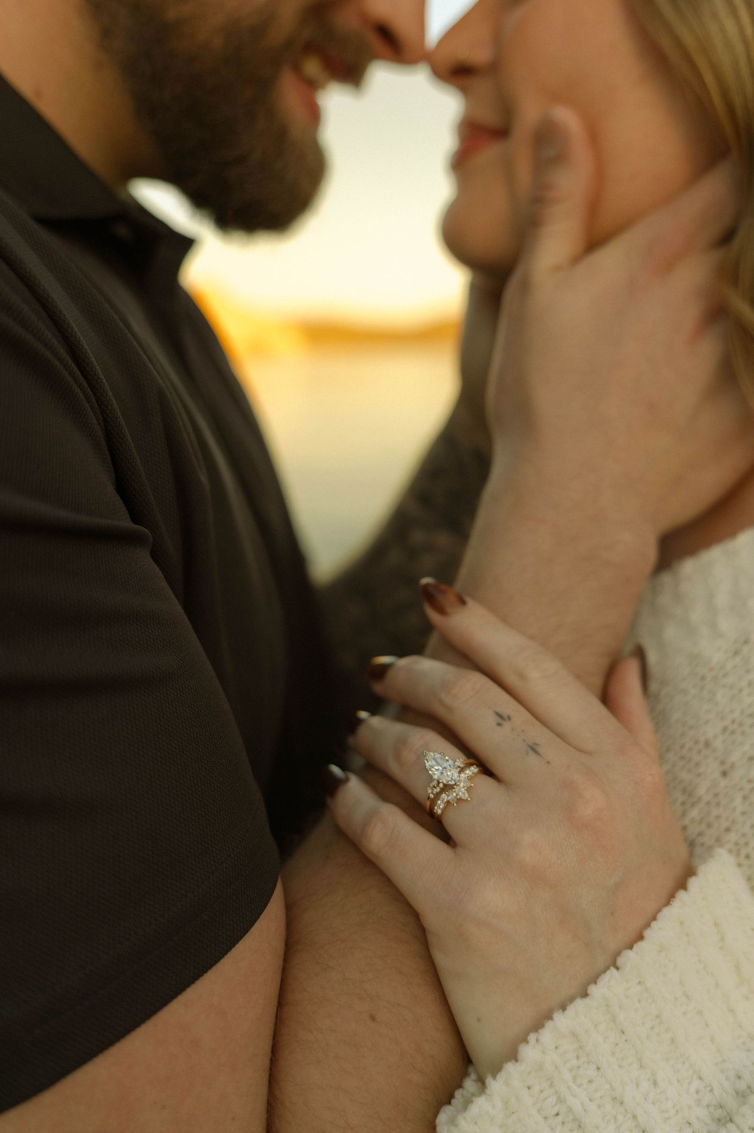 A close-up romantic moment showing hands with an engagement ring during a sunset proposal.