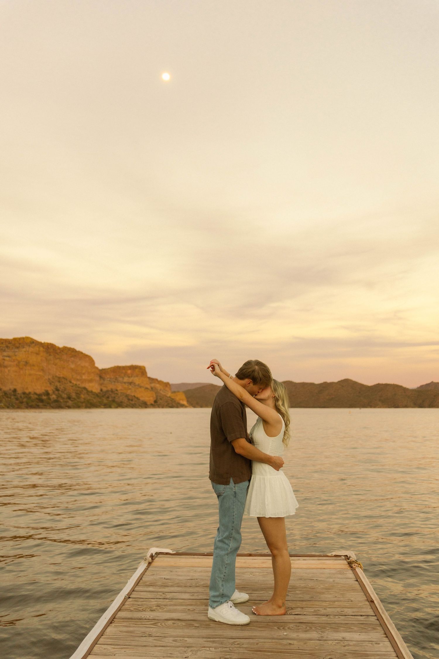 Two people share an intimate moment on a dock during golden hour.
