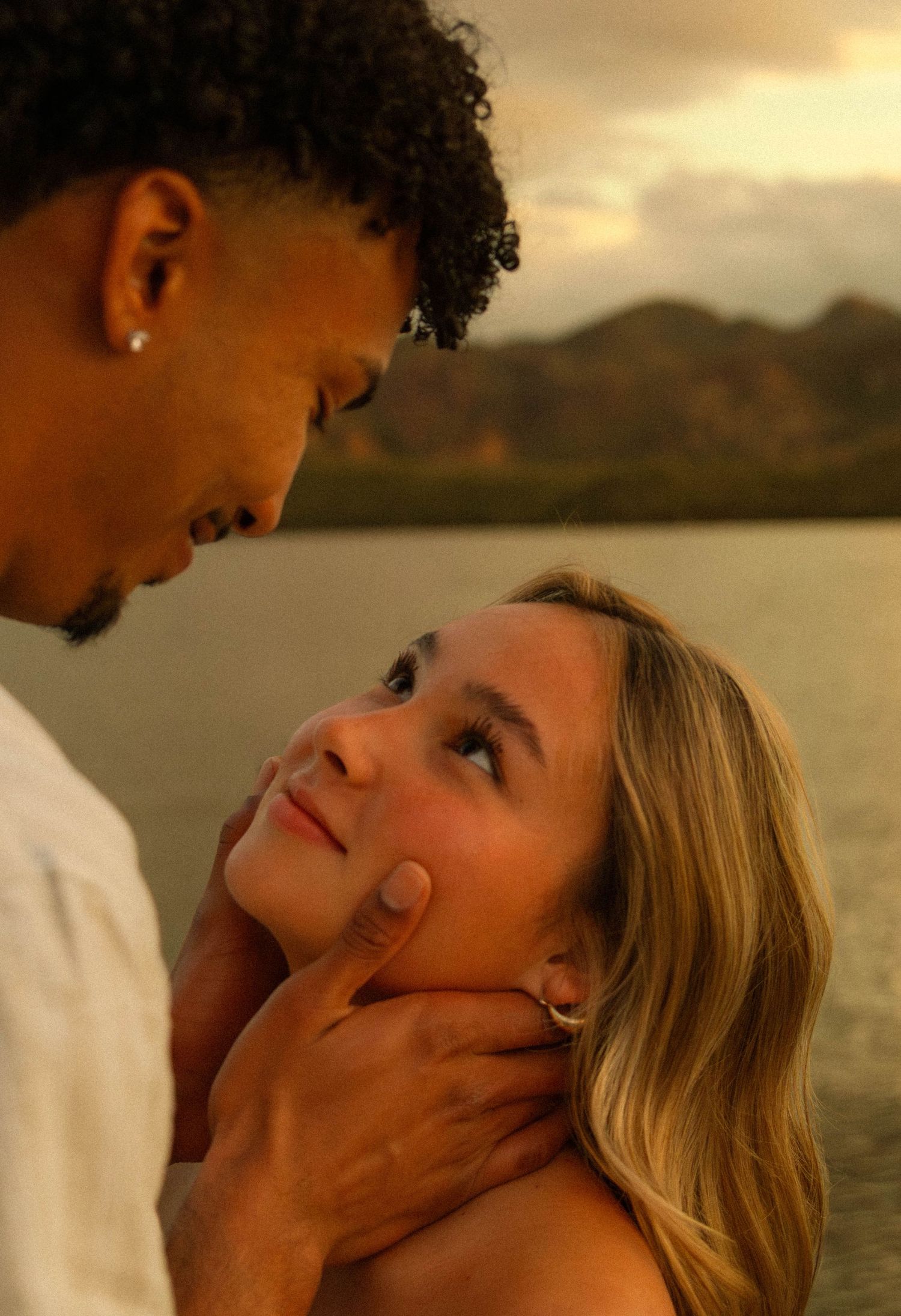 An intimate moment between a couple by a lake with mountains and warm sunset lighting.