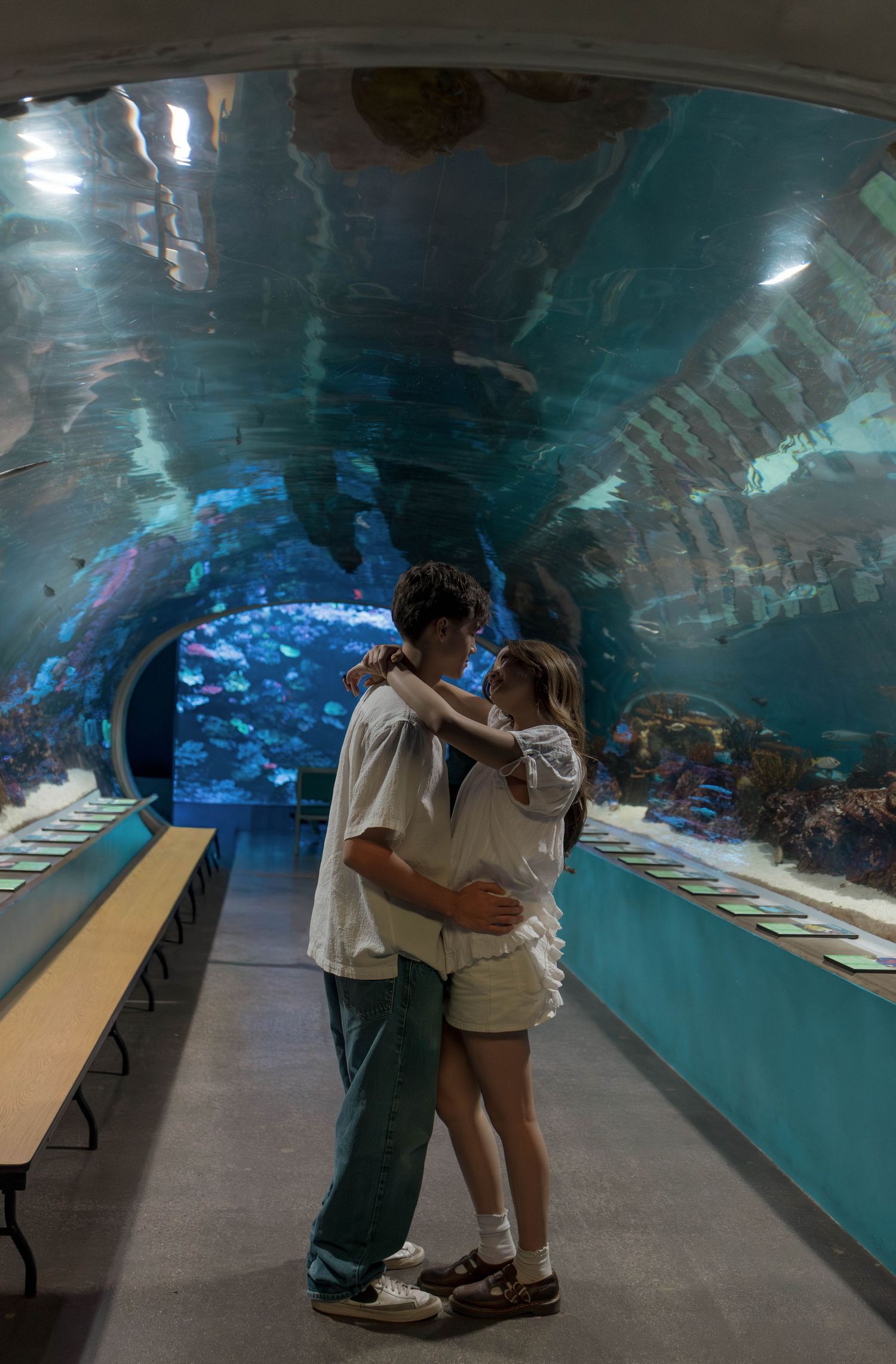 Couple shares a romantic moment in front of illuminated aquarium tanks.