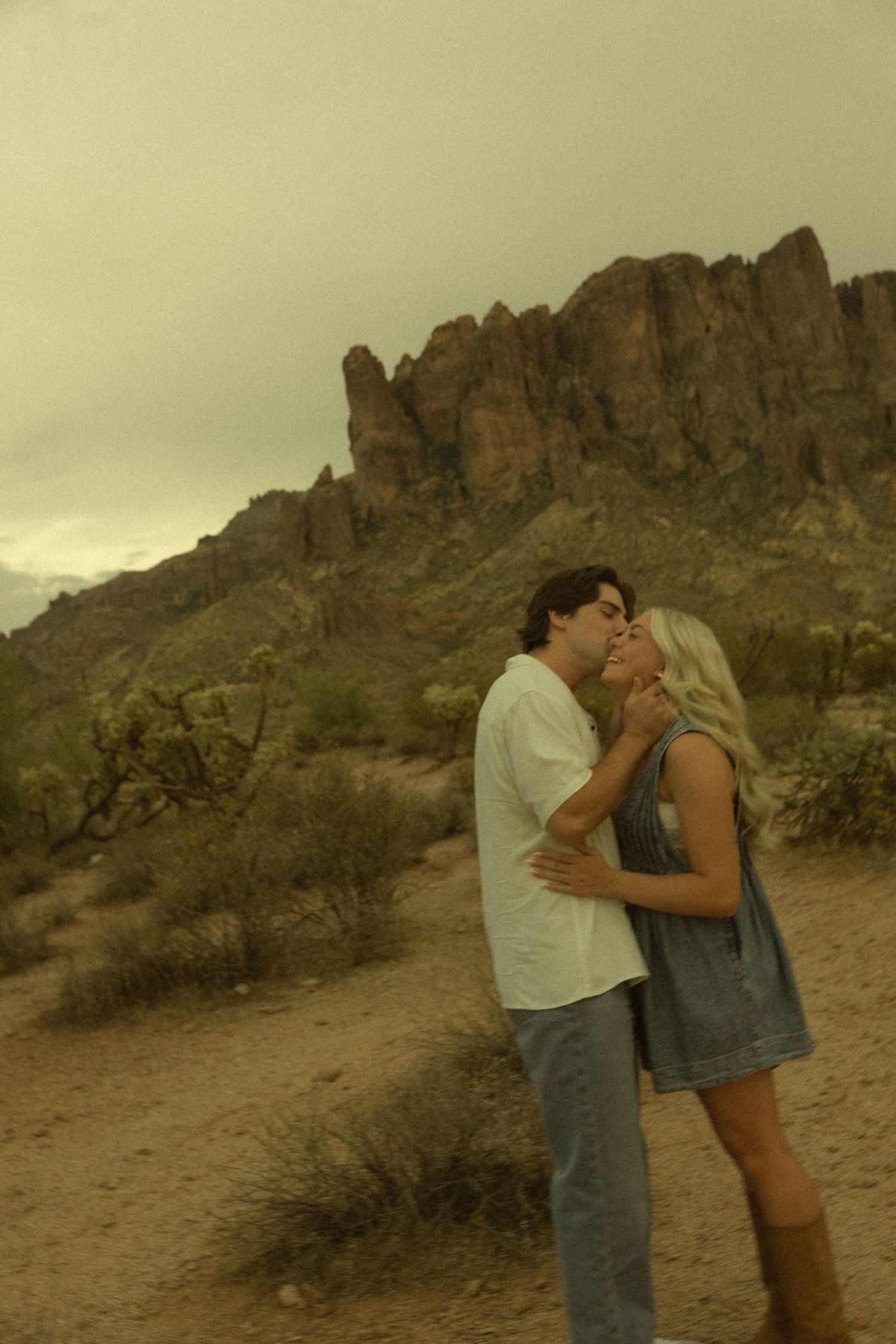 Couple kissing in Arizona desert with dramatic rocky Superstition Mountains backdrop.