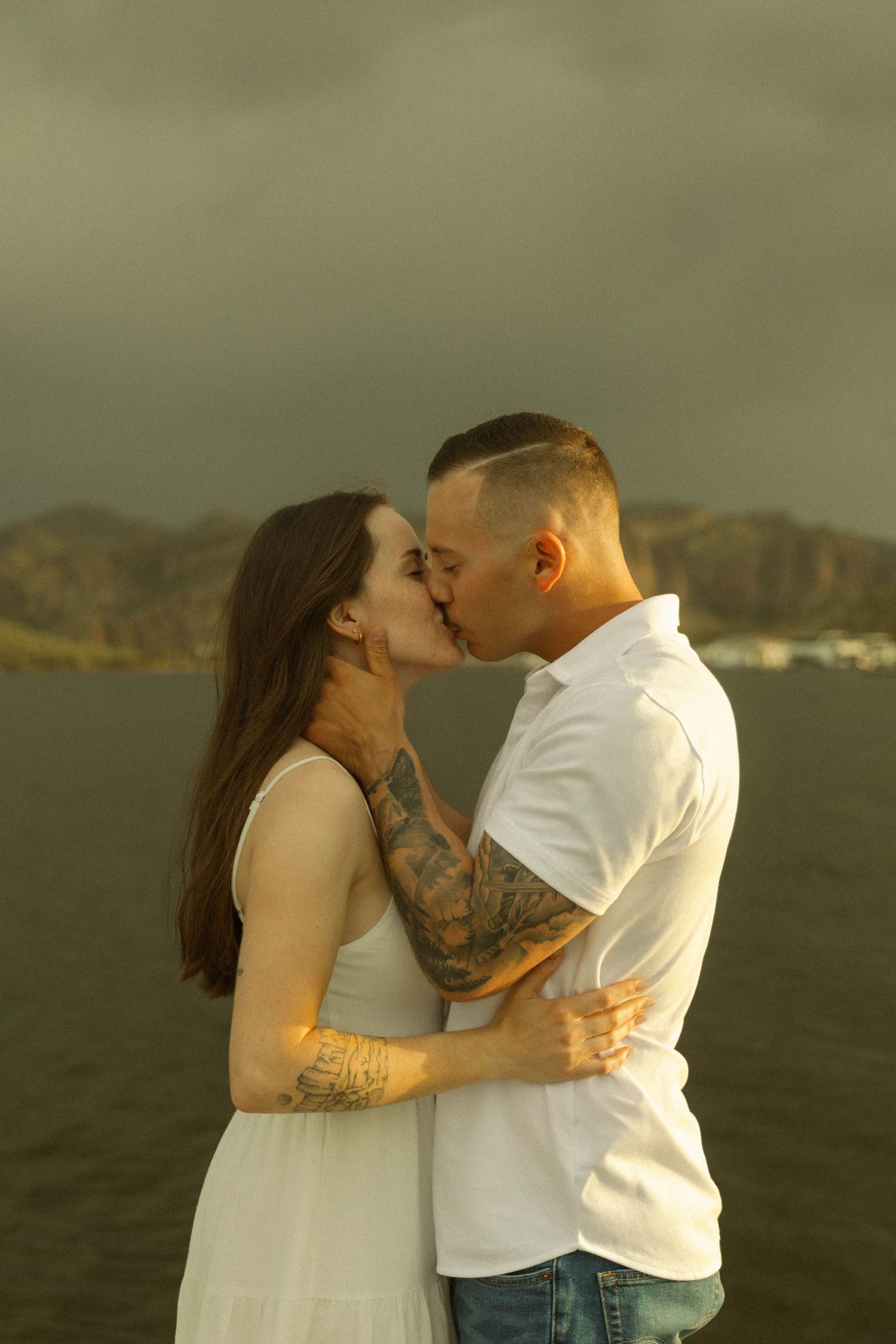 Romantic couple sharing a tender kiss against a scenic mountain backdrop at sunset.