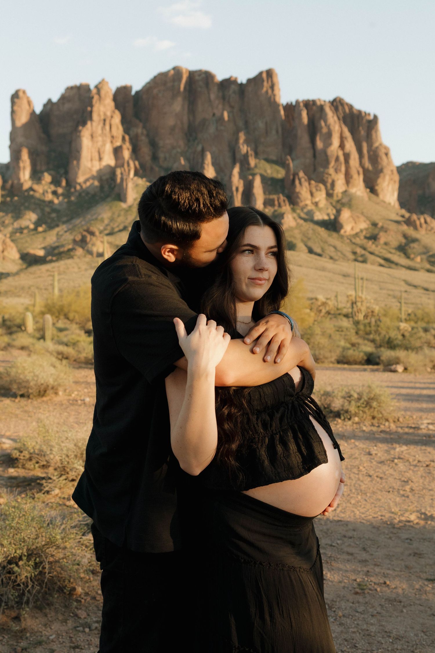 A romantic couple embraces against a backdrop of majestic desert rock formations during golden hour.