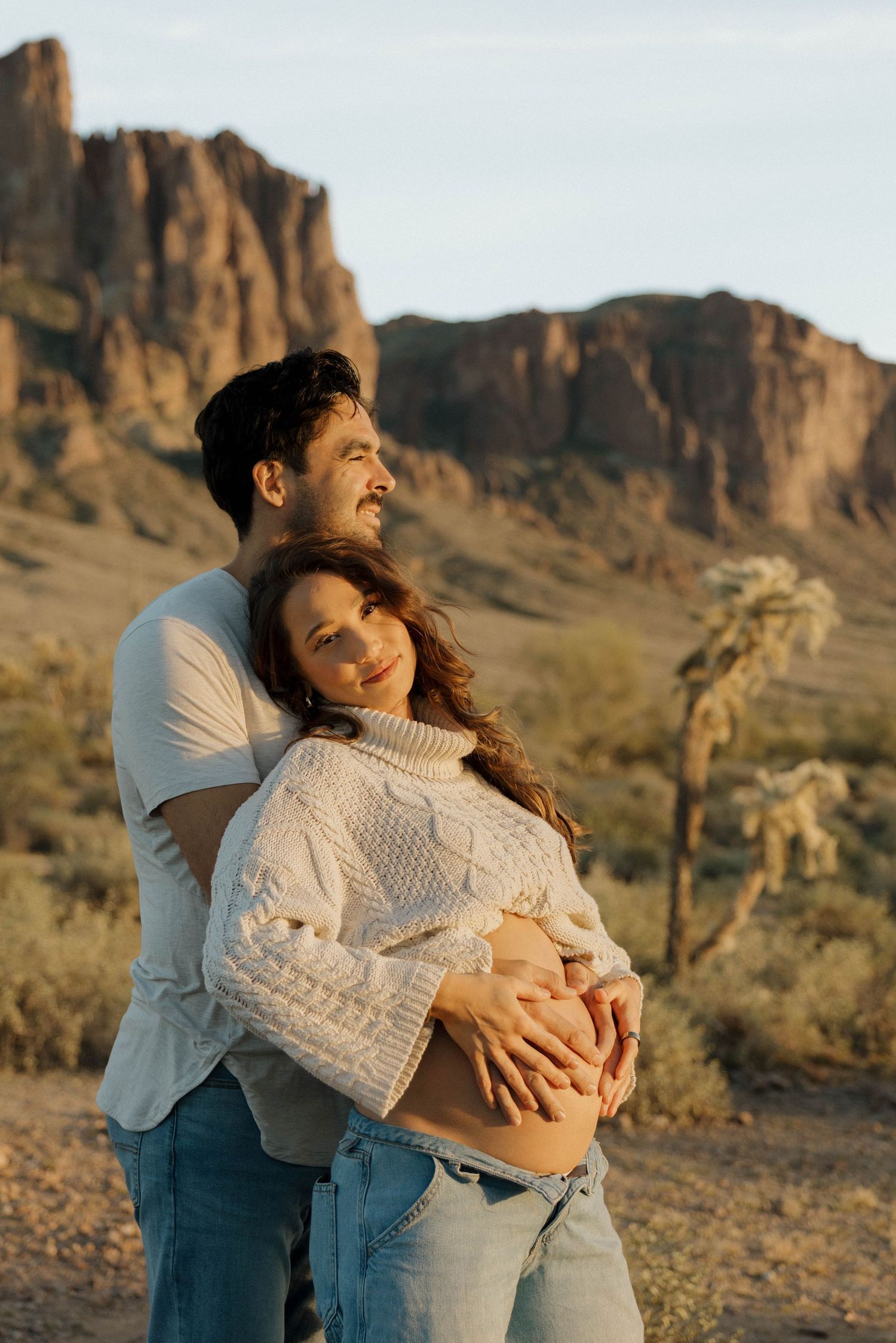A couple embraces in front of rugged desert mountains during golden hour at Superstition Mountains.