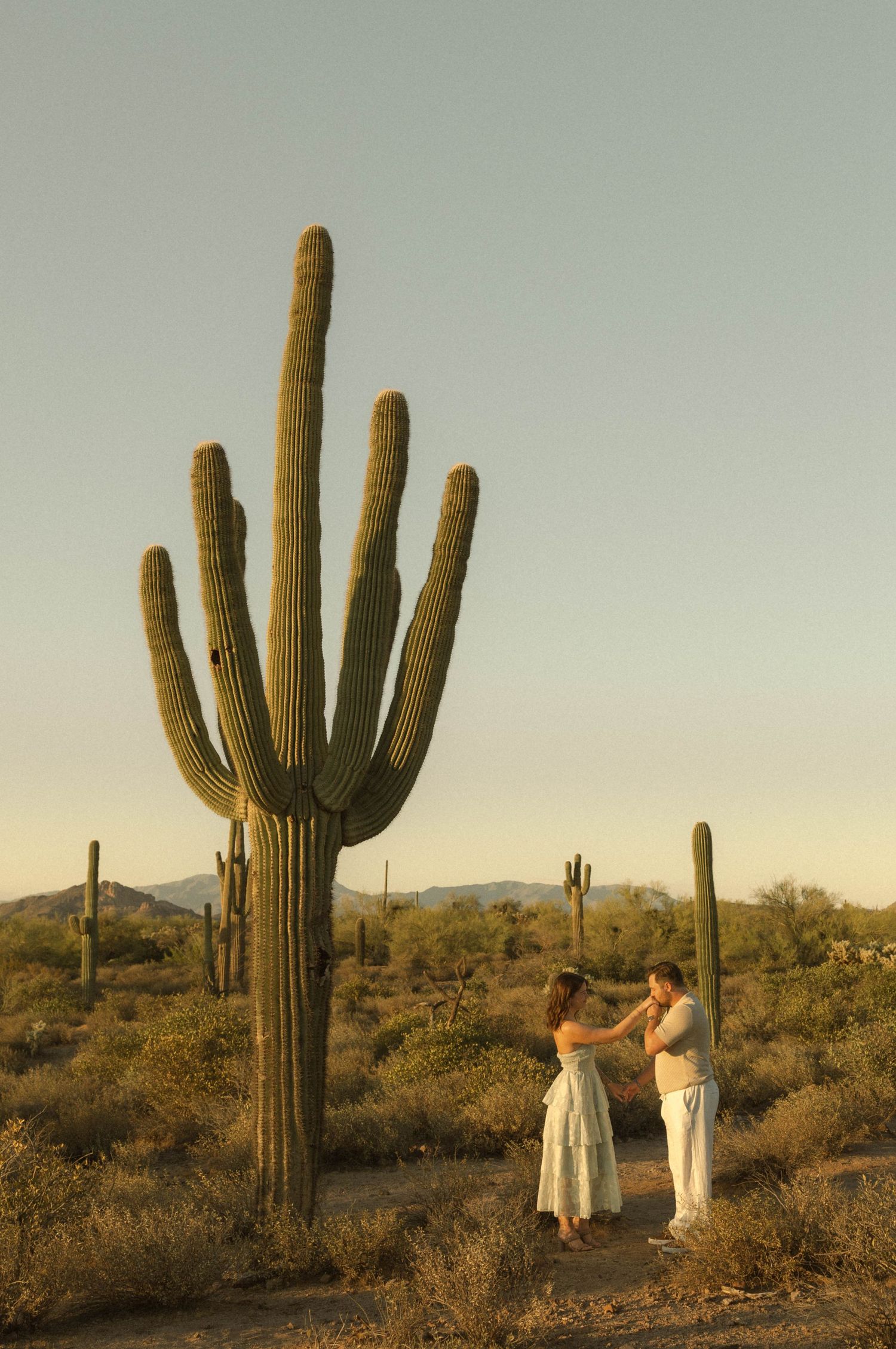 Couple dancing near a tall saguaro cactus in the Sonoran Desert at golden hour with mountains in the background.