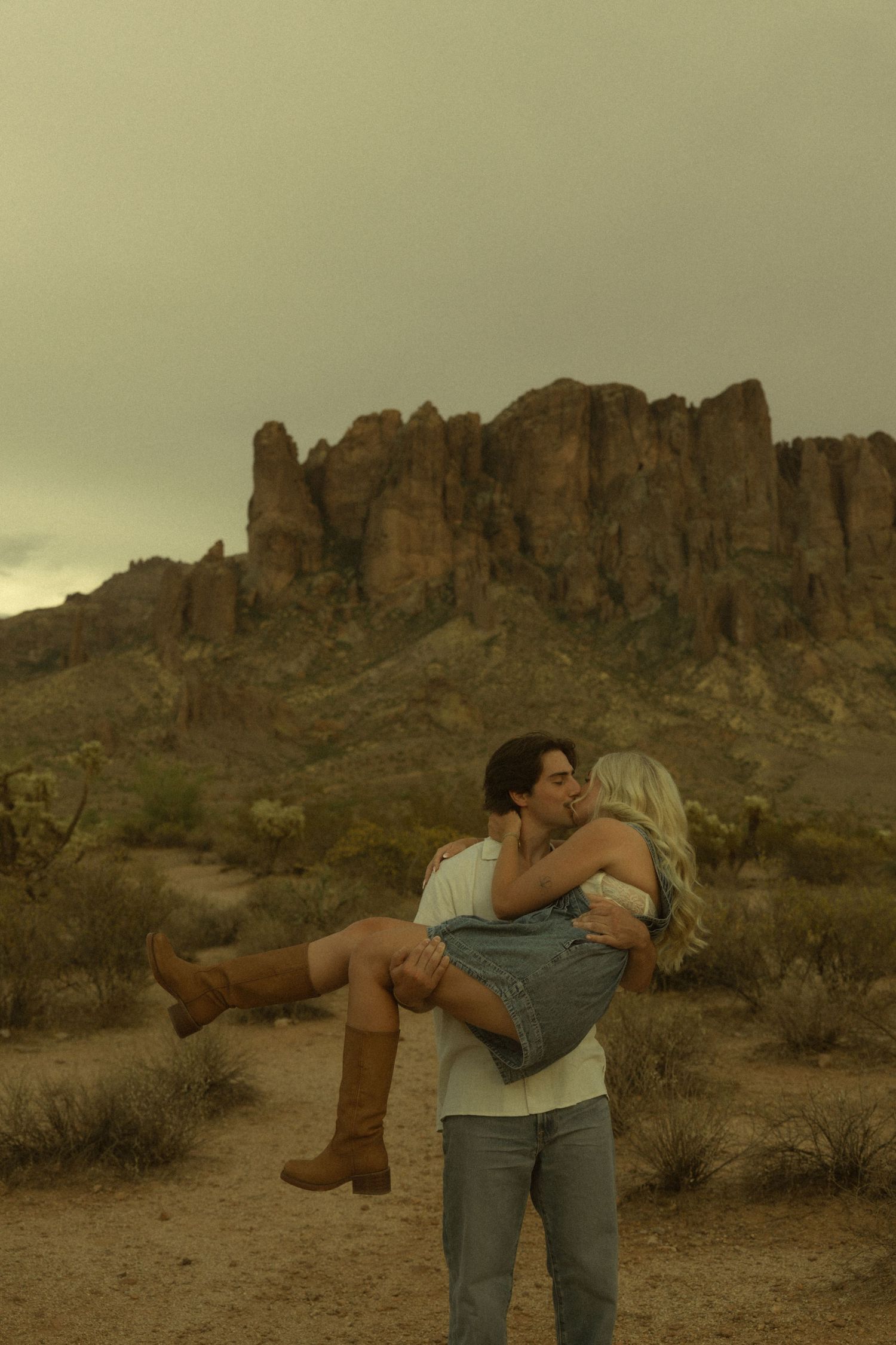 Man lifting and kissing woman in front of rocky Superstition Mountains in desert.