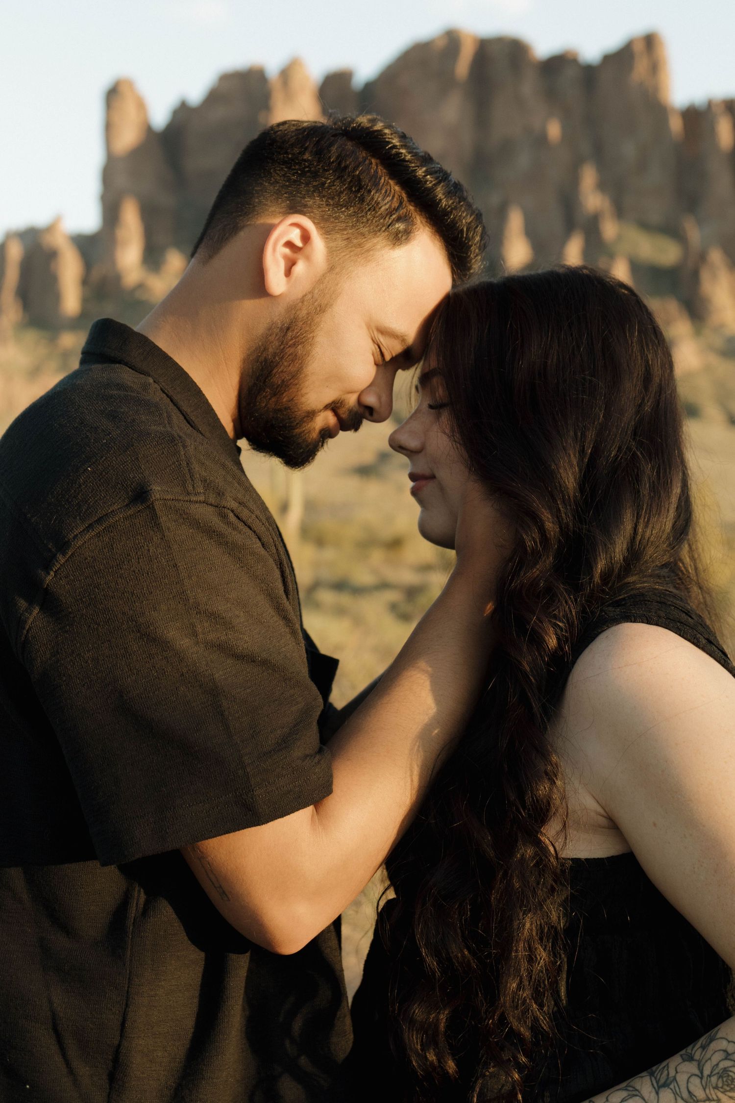 An intimate couple shares tender moments in front of towering desert cliffs at sunset.