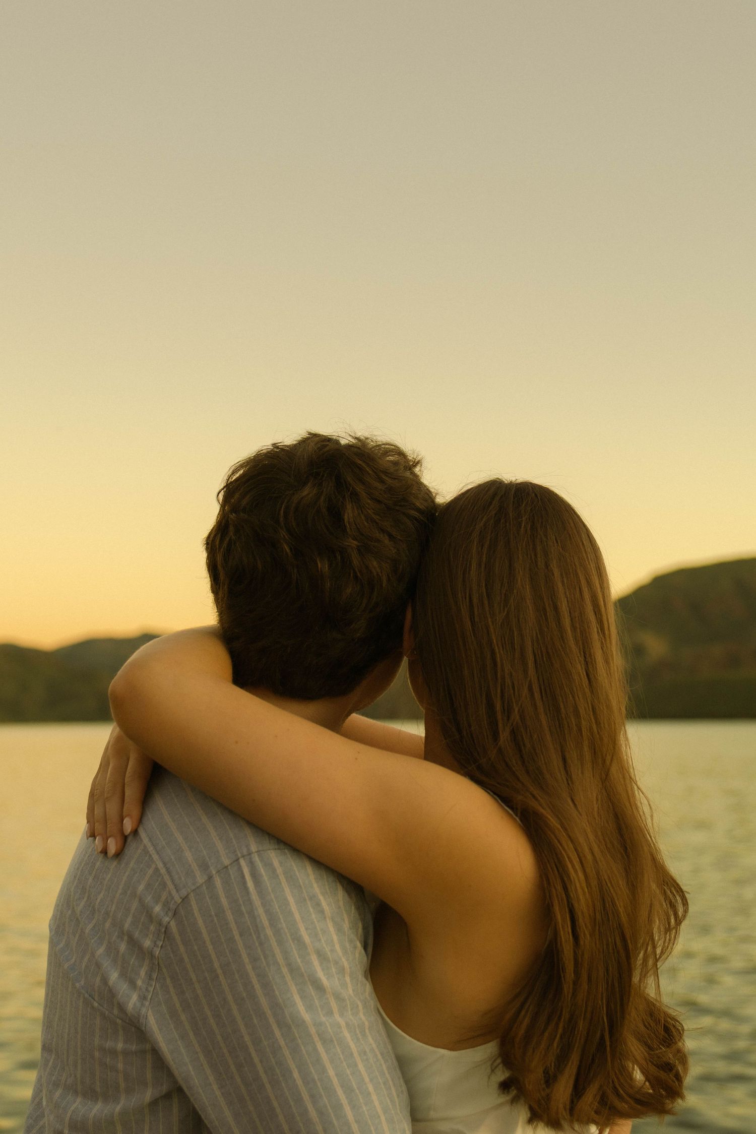 Couple embracing while watching sunset over a peaceful lake with mountains in the distance.