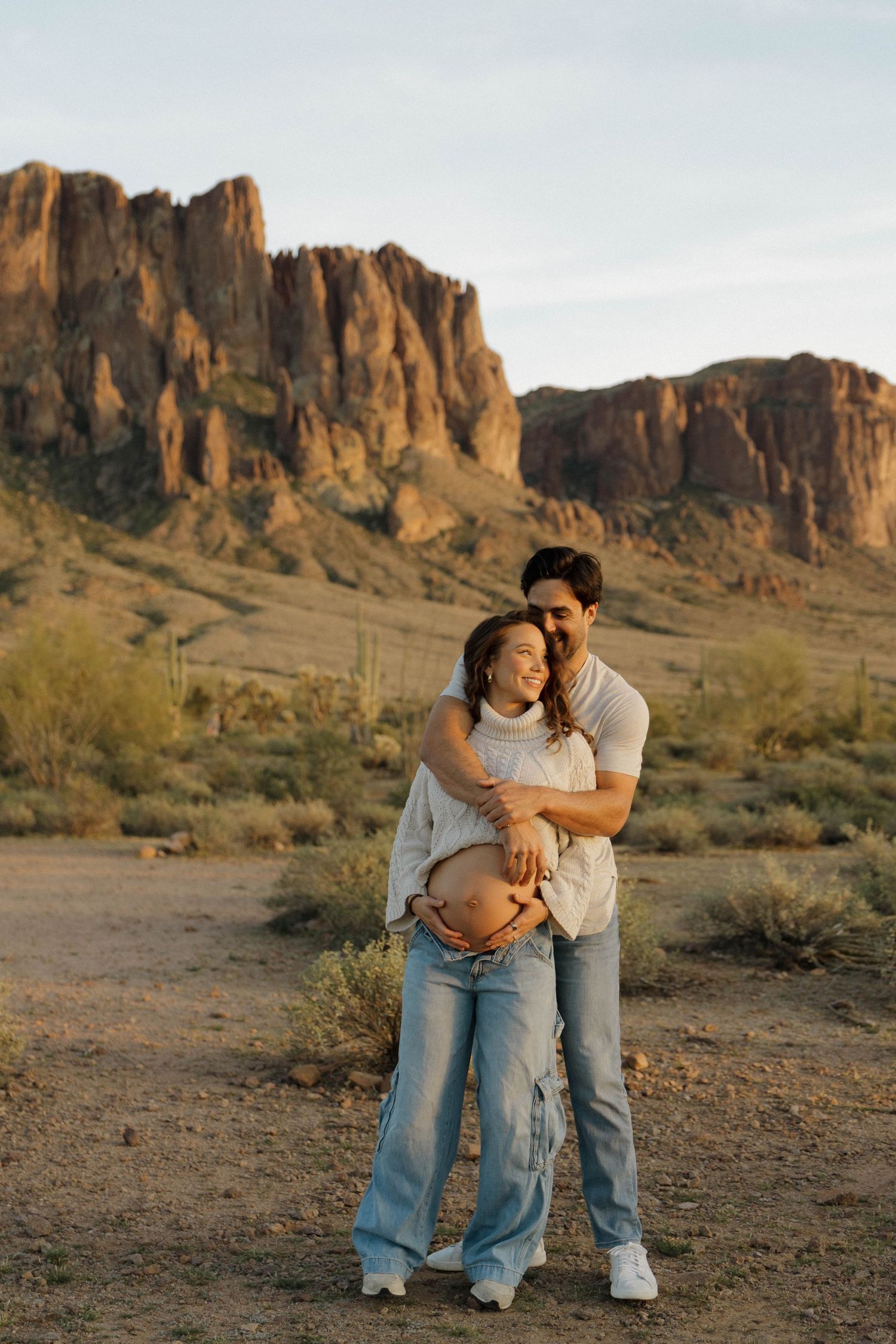 A tender moment captured between a couple sitting in front of majestic desert cliffs.