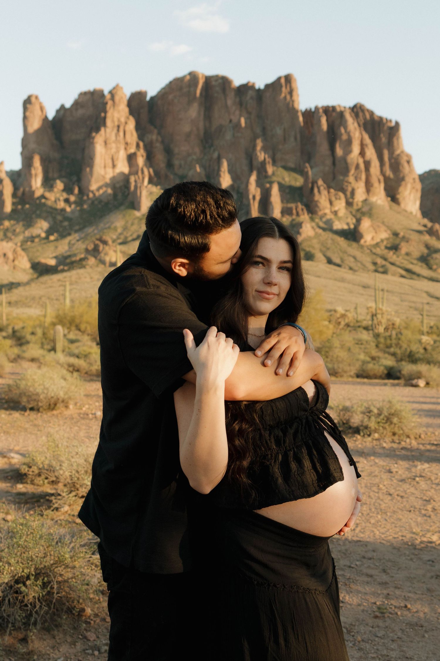 A romantic maternity photo shoot in front of majestic desert rock formations during golden hour.