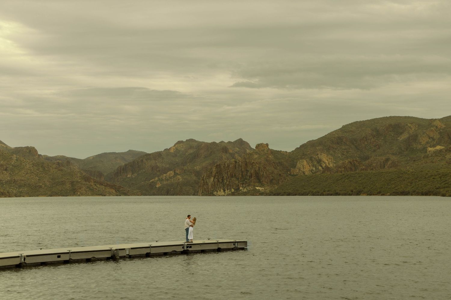 A scenic panoramic view of mountains and a lake under moody cloudy skies at dusk.