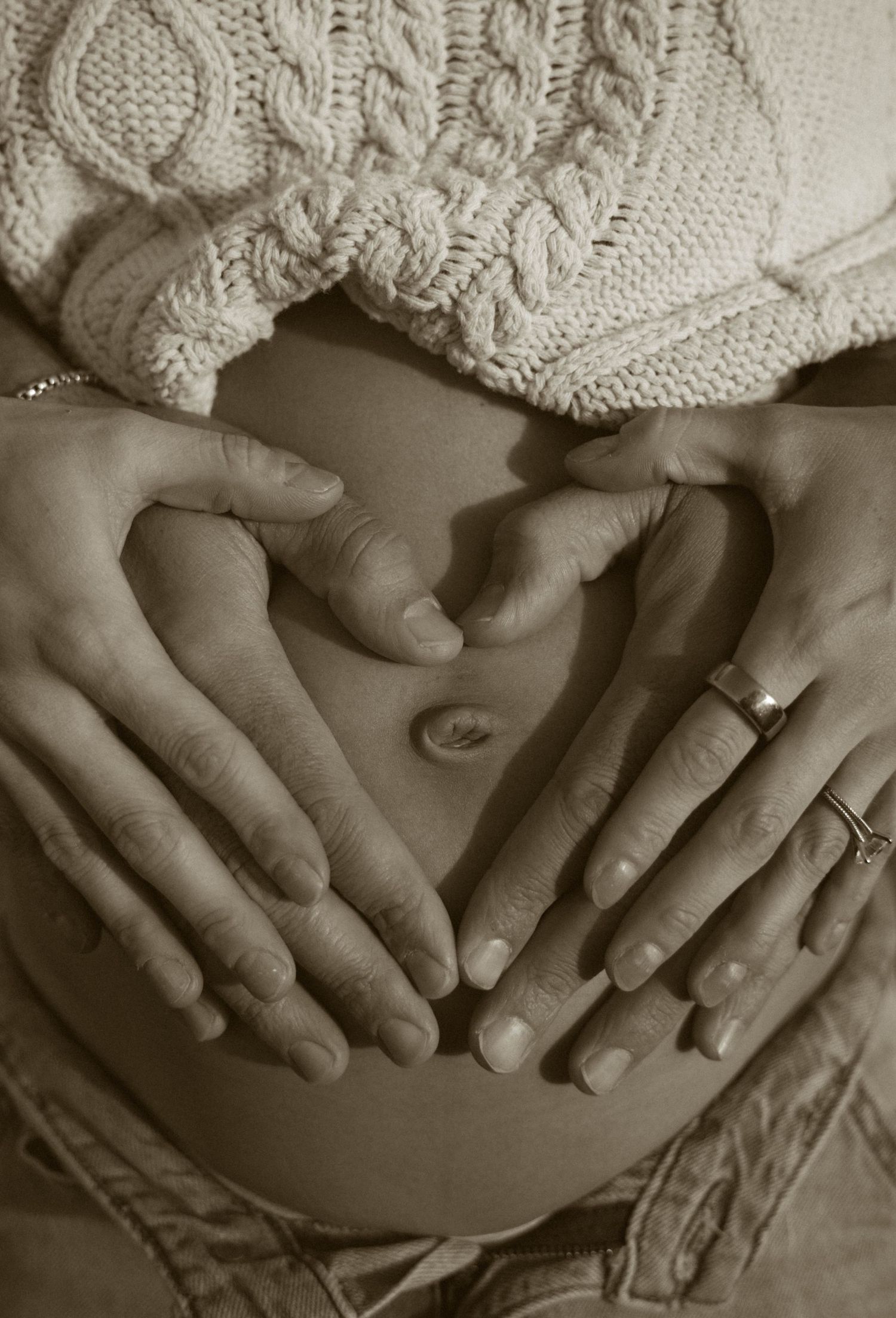 A series of hands gently resting on a pregnant belly, shown in black and white with soft knit fabric.
