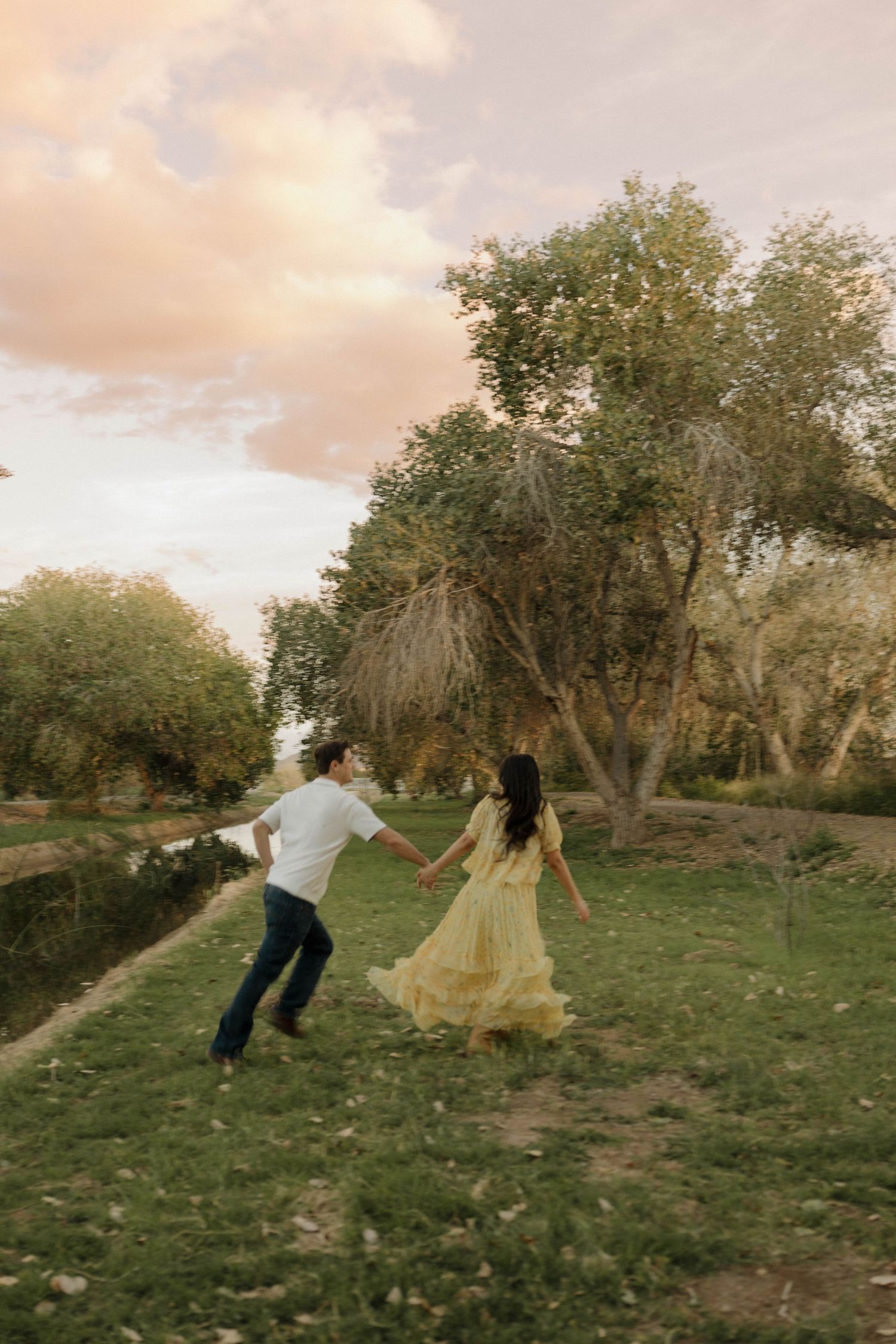 Playful couple dancing and spinning in sunset lit park.