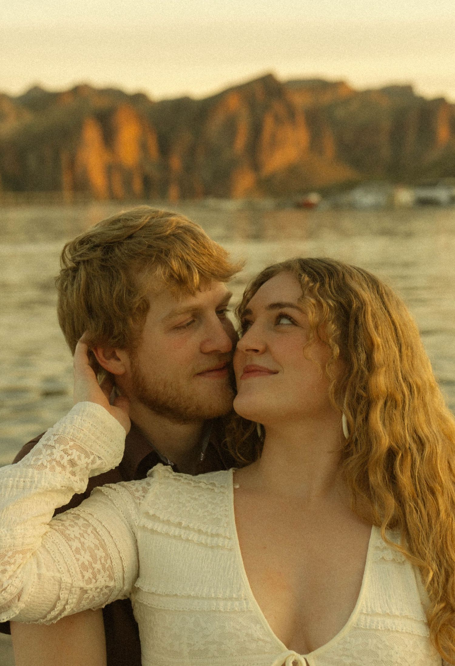 Intimate moment between couple against backdrop of mountains and water during golden hour.