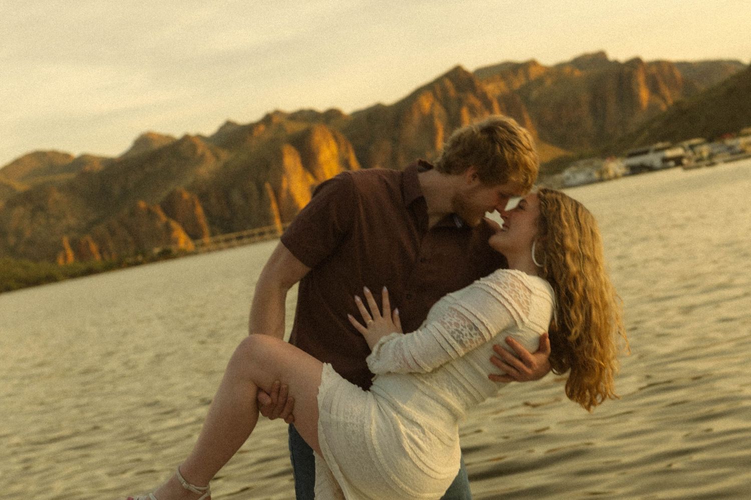 Silhouetted couple embracing and kissing at sunset by a scenic mountain lake.