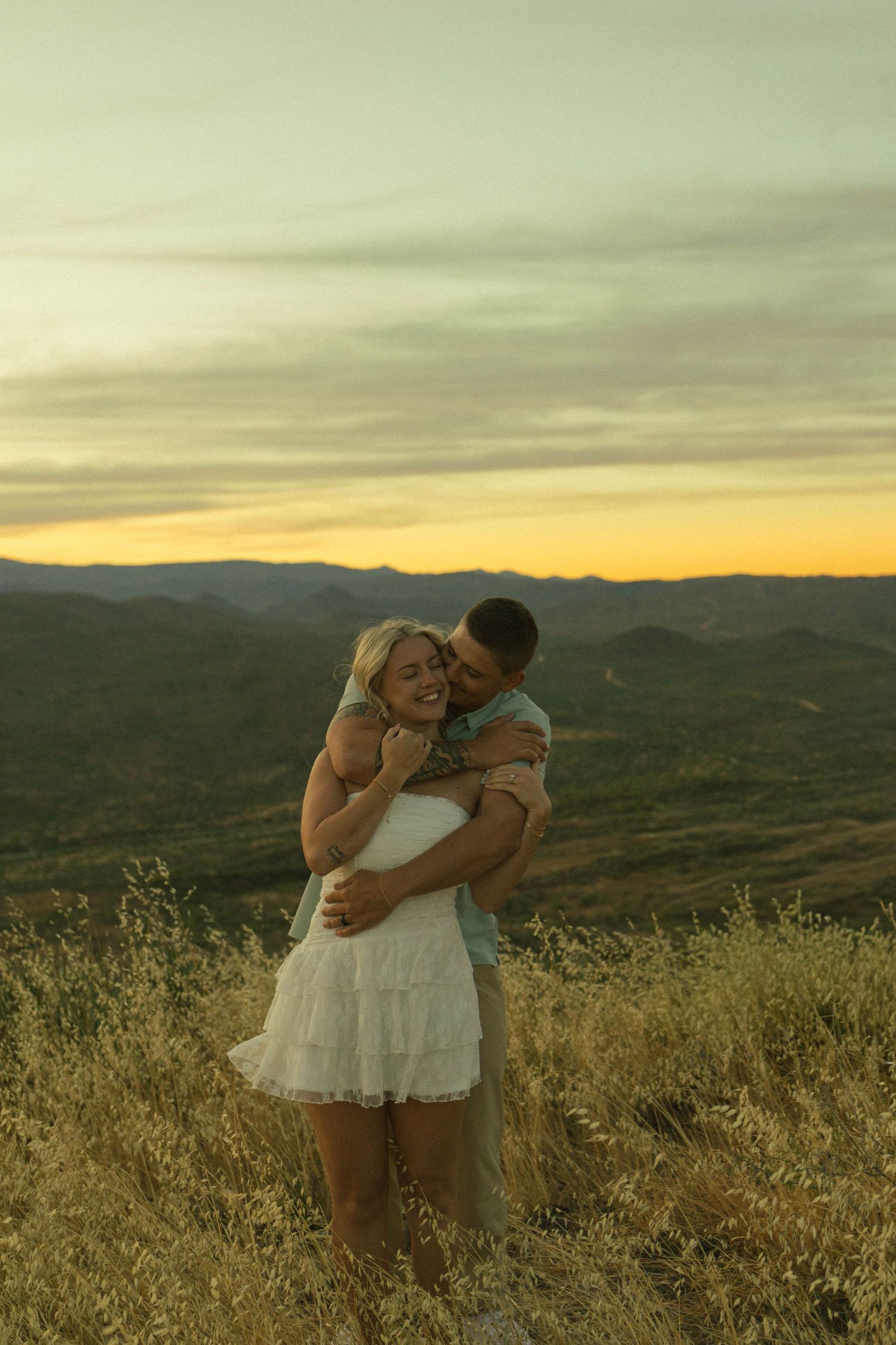 Happy couple hugging and laughing in golden field during vibrant sunset.