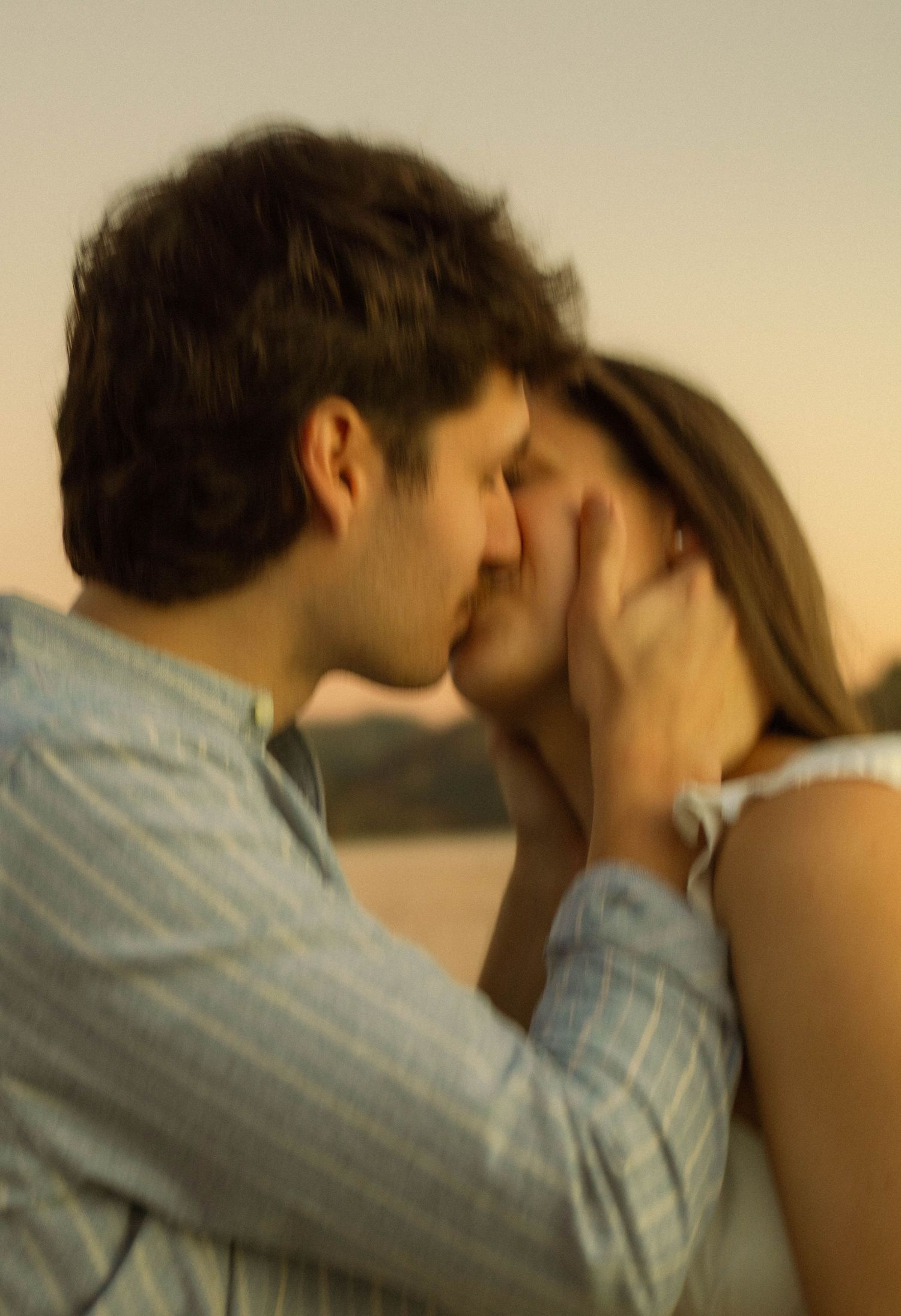 A tender romantic moment shared between two people against a sunset backdrop.