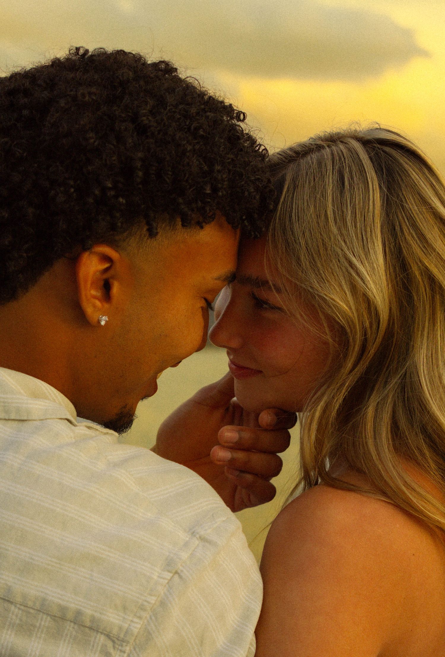 A couple shares an intimate moment at sunset with a warm golden glow in the background.