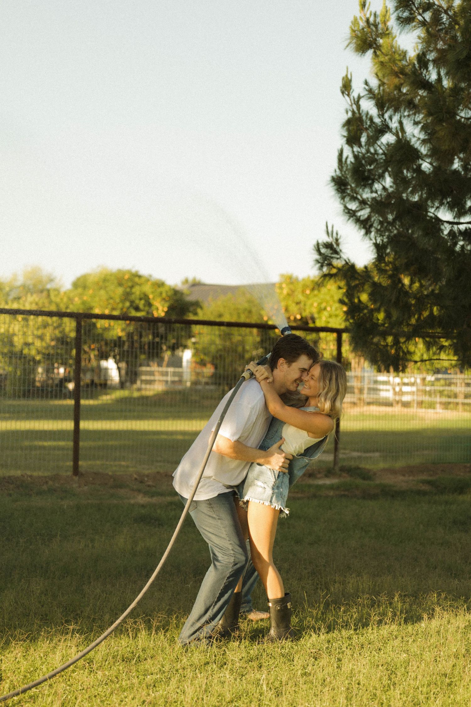 A couple shares a tender embrace while dancing together on a lush green lawn at golden hour.