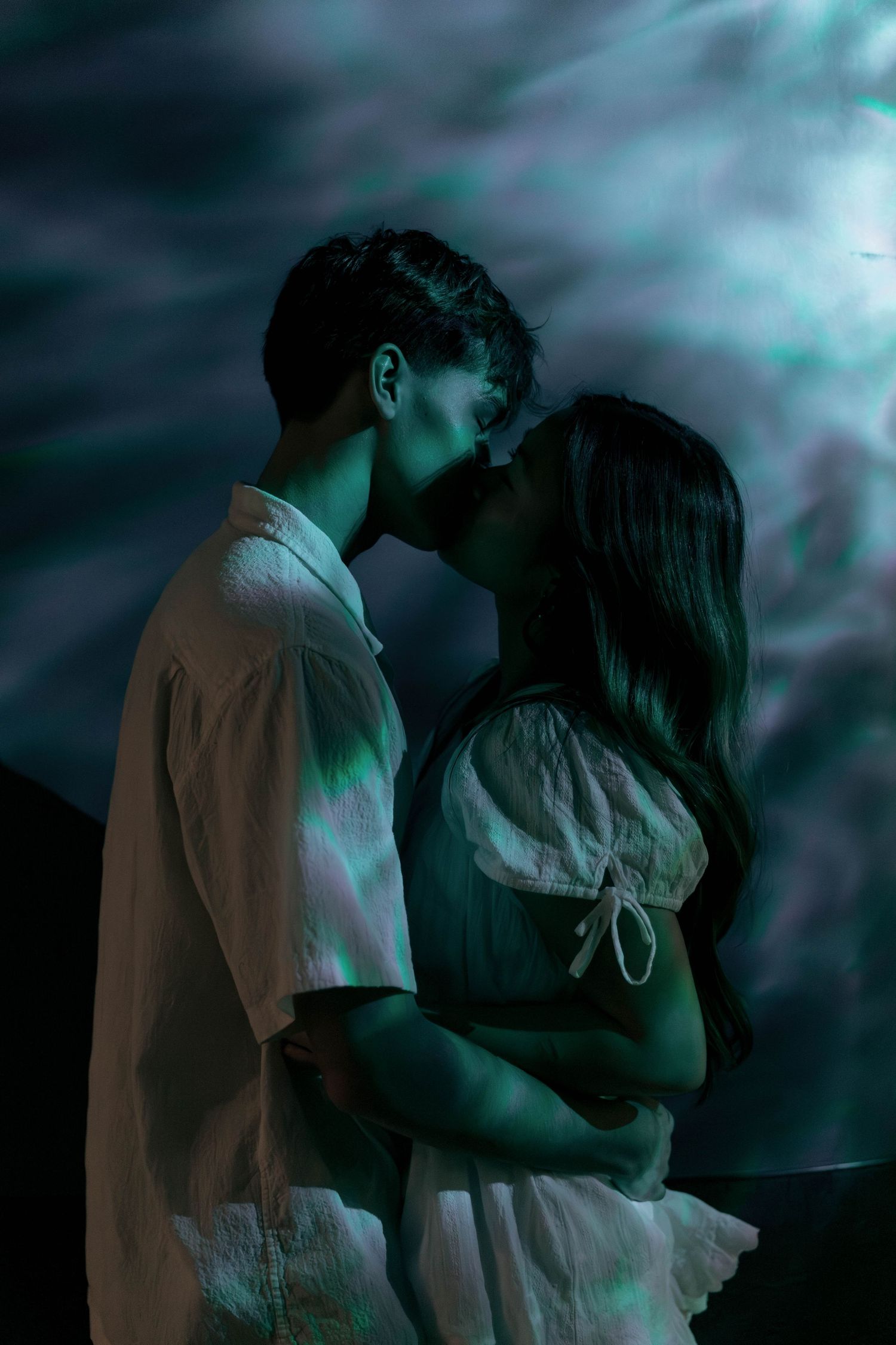 A romantic couple embraces in silhouette against a moody teal-colored night sky with dramatic clouds.
