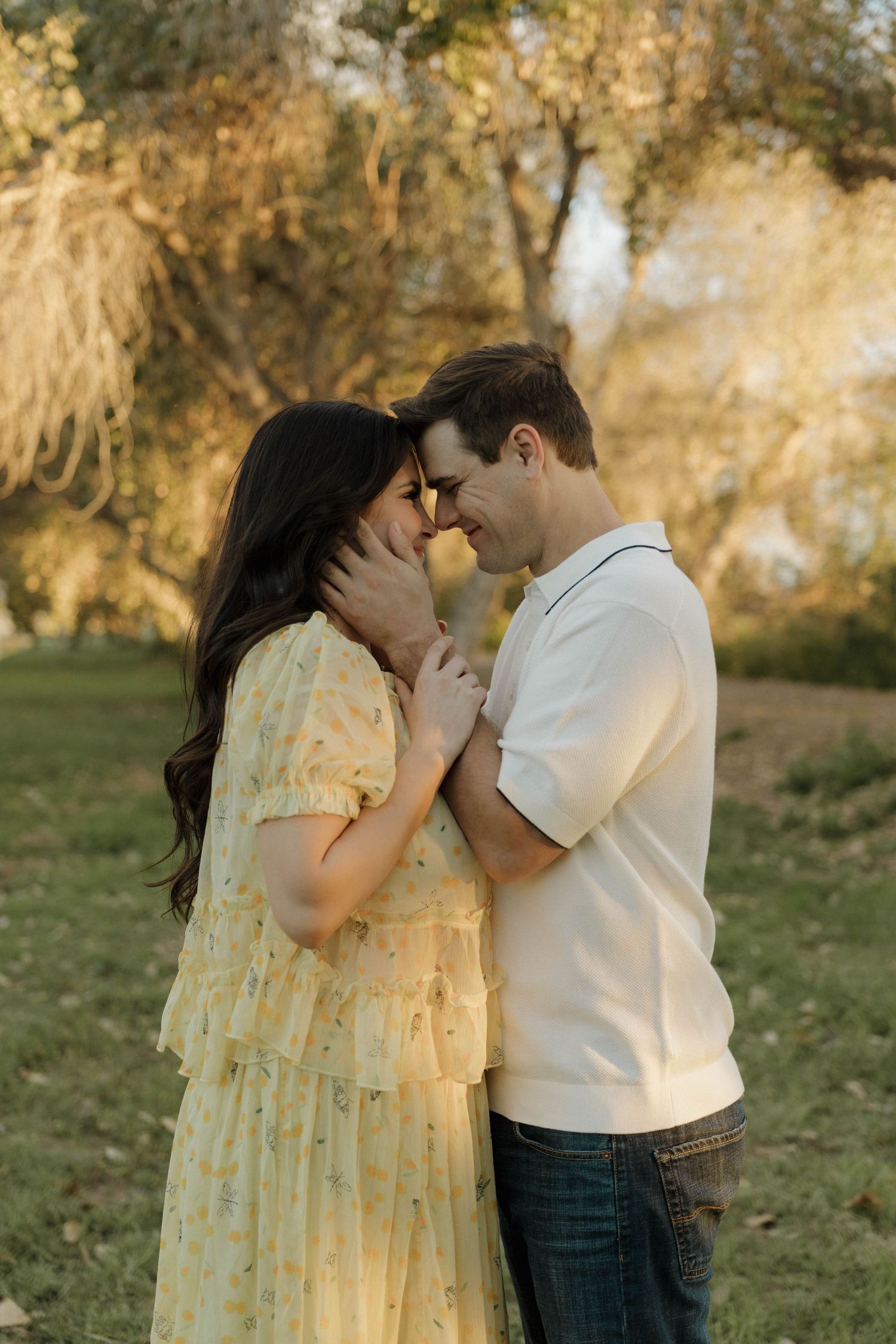 A couple shares tender moments in a yellow dress and white shirt on a grassy hillside.