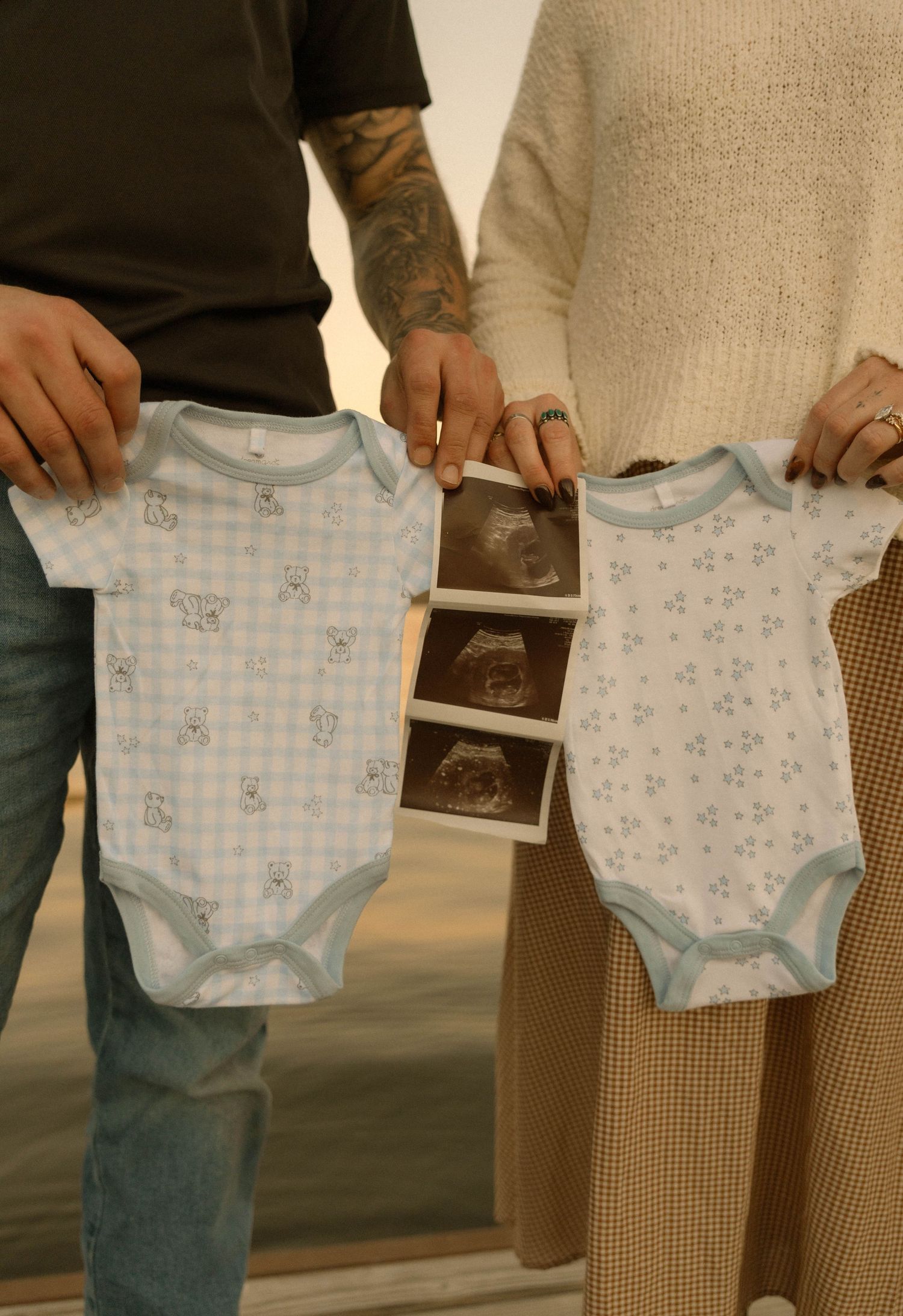 Couple holding baby onesies and ultrasound photos in sunset lighting.