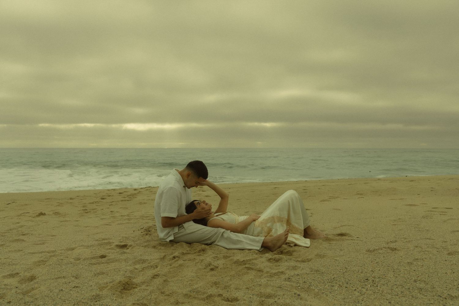 Couple sharing a romantic moment on a sandy beach under a cloudy sky at dusk.