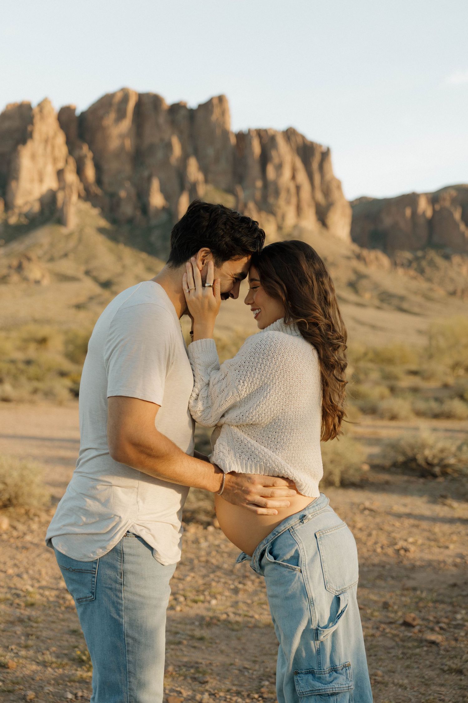A romantic couple embraces in front of majestic desert cliffs during golden hour at Superstition Mountains.
