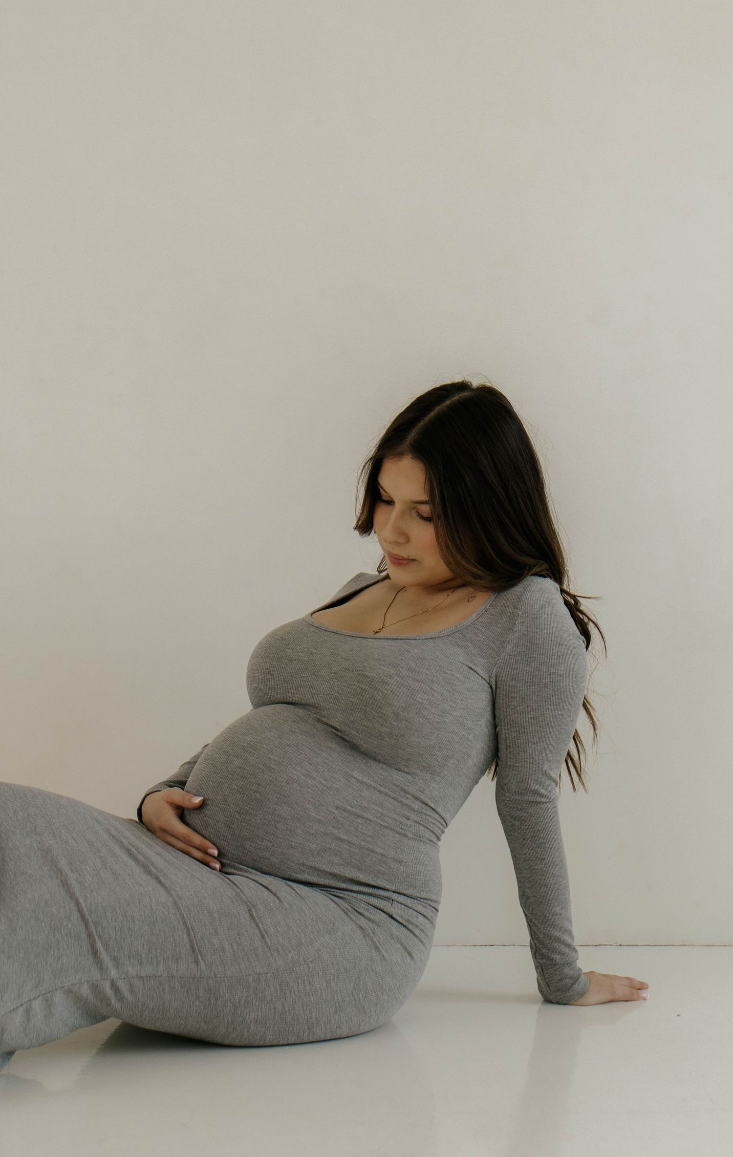 A sequence of artistic maternity poses showing a person in a gray dress lying on a white floor.