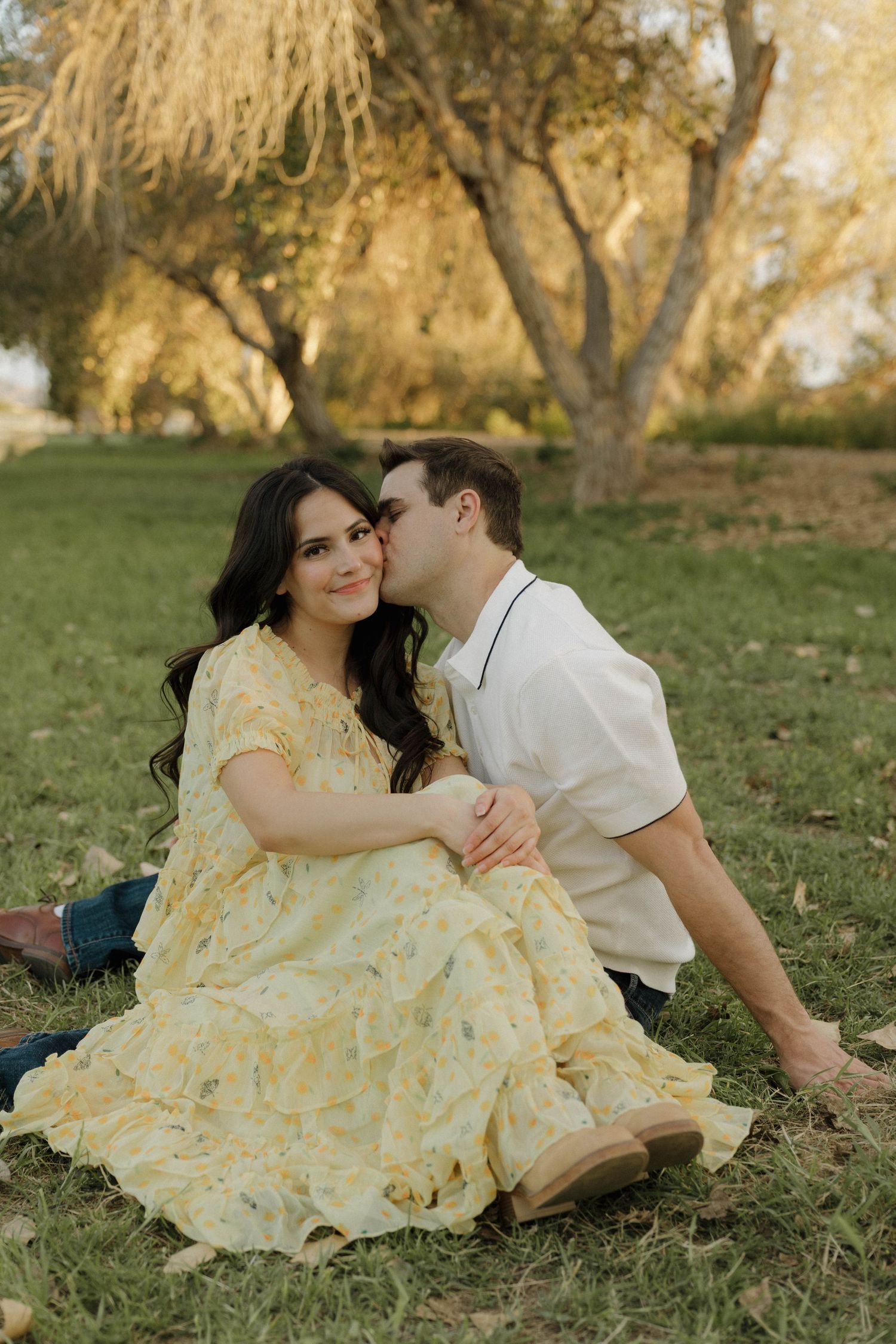 Intimate outdoor photoshoot with couple in yellow dress and white shirt on grassy hill.