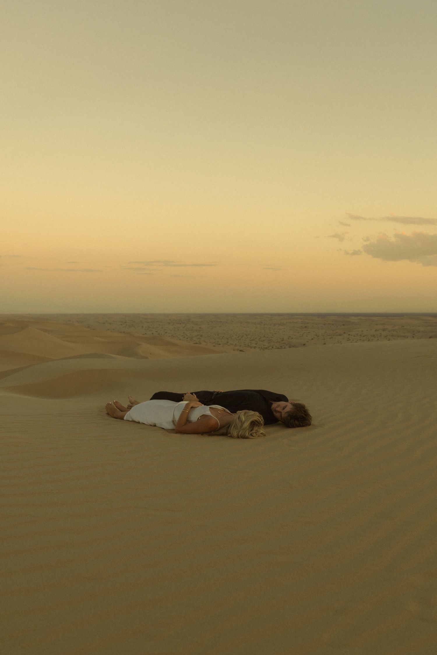Romantic couple lying together on golden sand dunes in a serene desert at dusk.