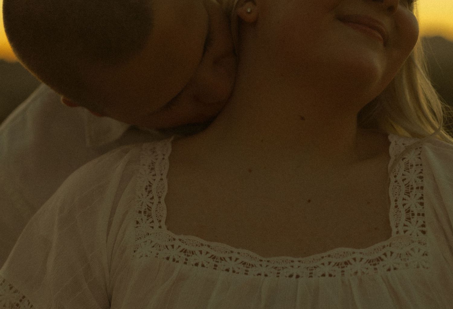 A couple shares a tender moment at golden hour, with a man kissing a woman's cheek as she smiles warmly.