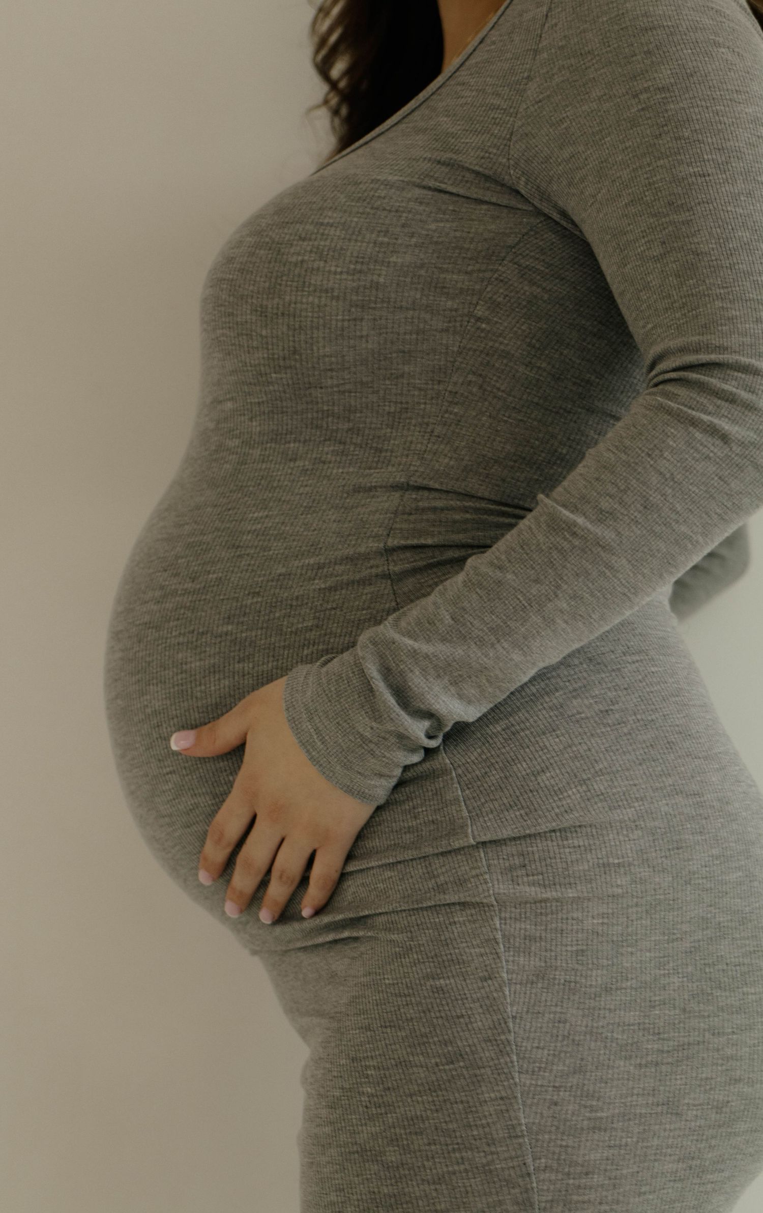 Side view progression of a growing baby bump shown in a grey maternity dress.