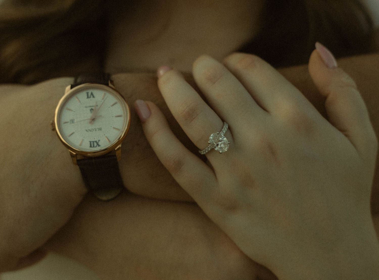 Close-up of a woman's hands wearing a rose gold watch and a sparkling diamond engagement ring.