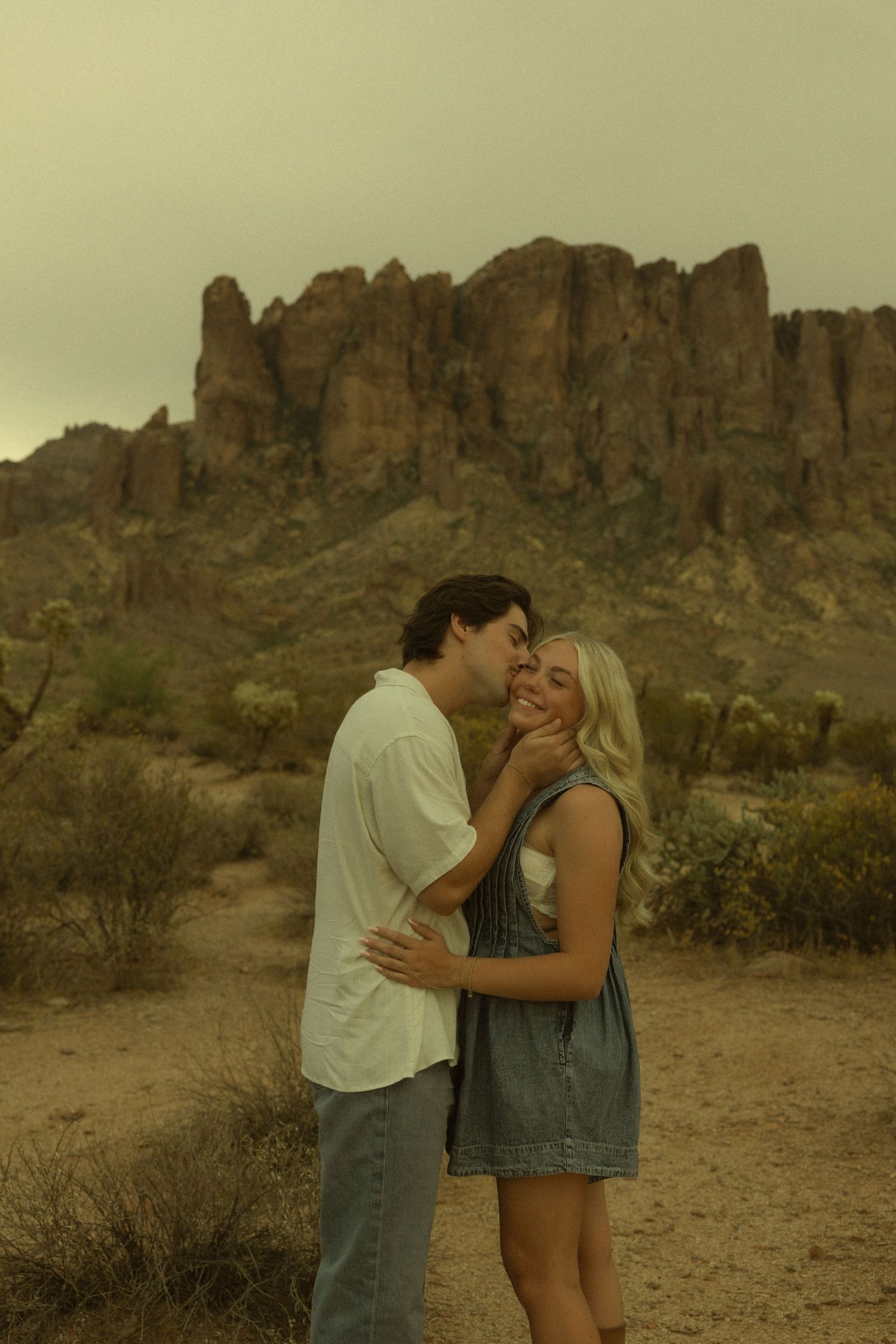 Man kissing woman on cheek before rugged Superstition Mountains in Arizona desert.