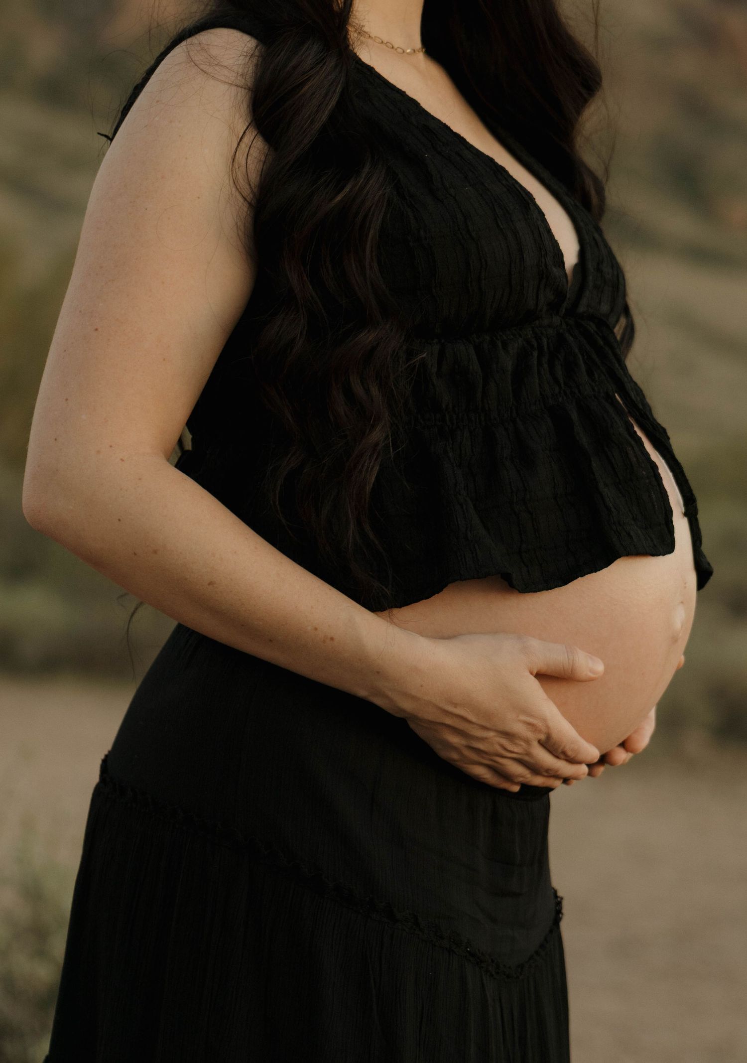 A close-up view of an expectant couple embracing, showing a pregnant belly against a desert backdrop.