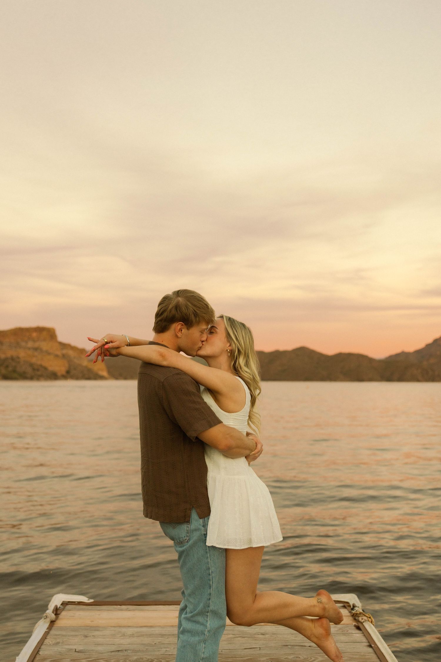 A couple dancing on a lakeside dock during a beautiful sunset.