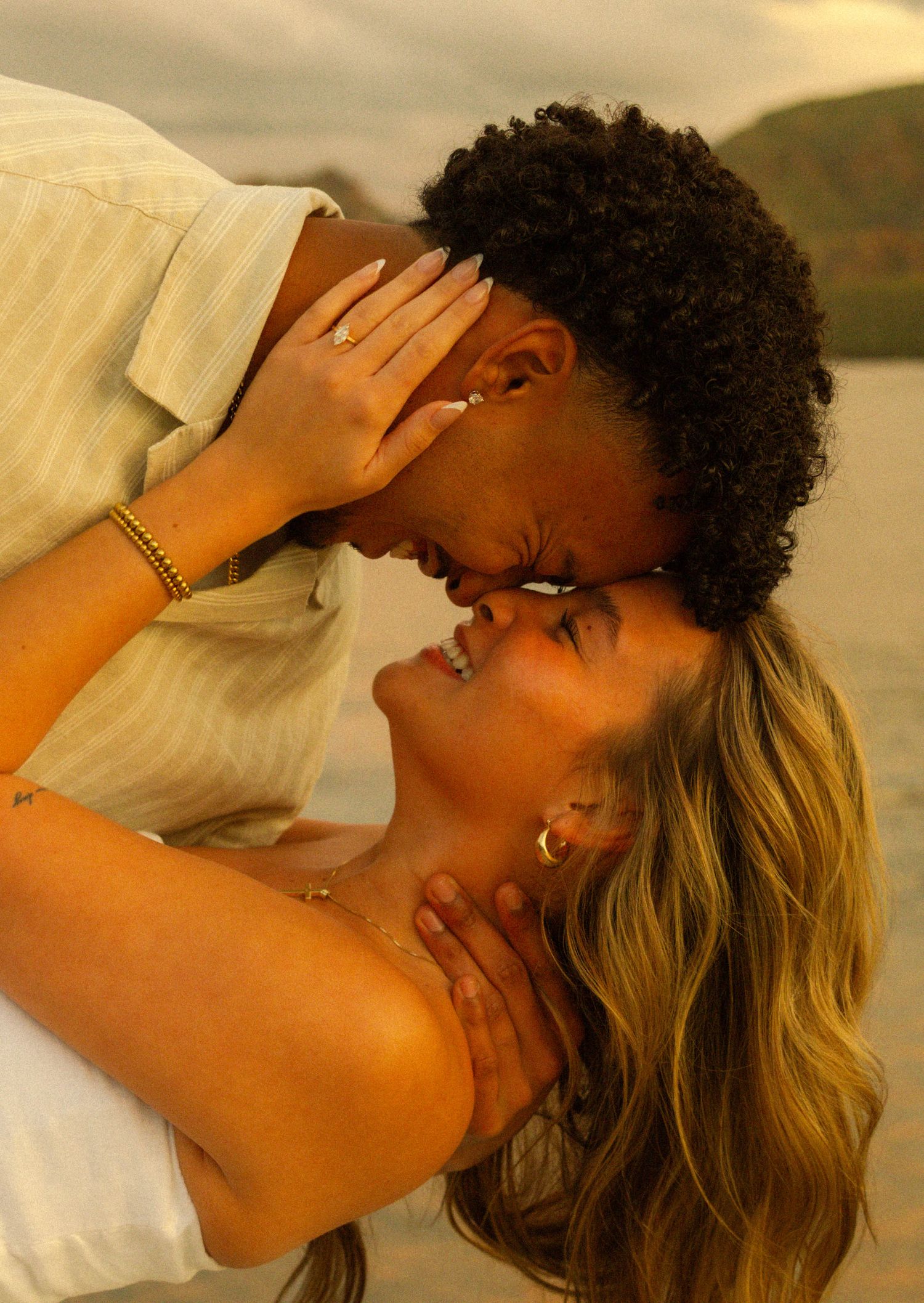 Romantic couple sharing an intimate moment on a deck during sunset with mountains in the background.